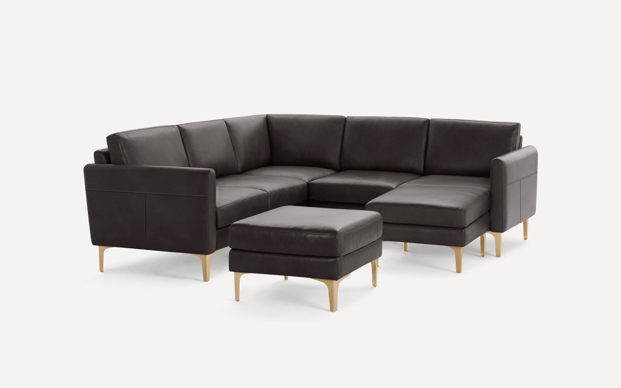 Dark gray leather sectional sofa with matching ottoman, featuring gold-toned metal legs and modern, clean lines.