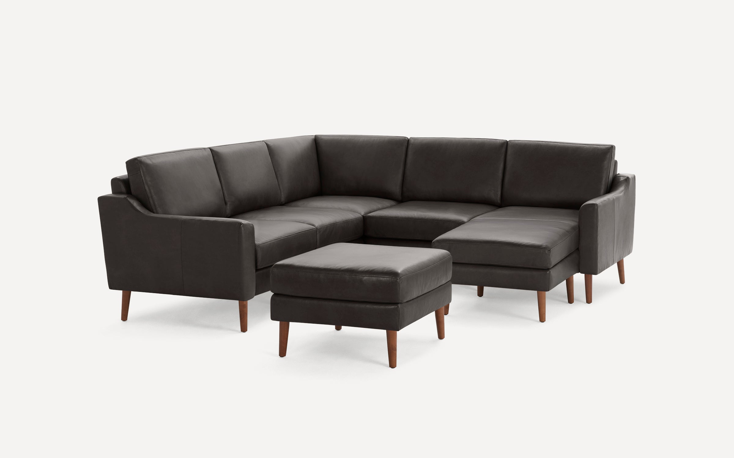 Dark brown leather sectional sofa with wooden legs and matching ottoman, modern and minimalist design.