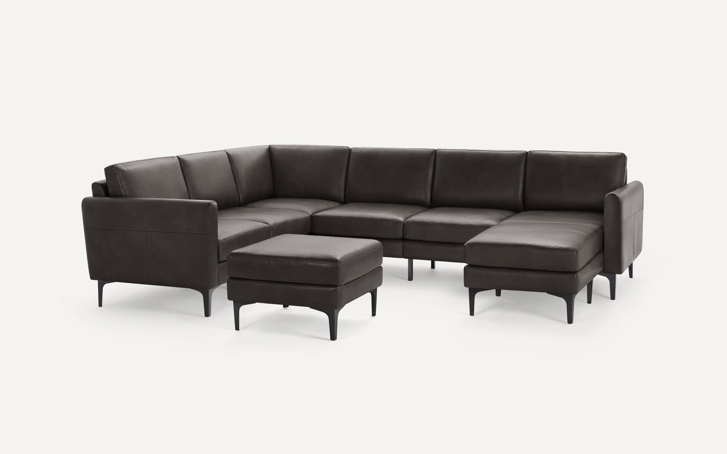 Dark gray leather sectional sofa with matching ottoman, sleek black legs, and modern, minimalist design on white background.