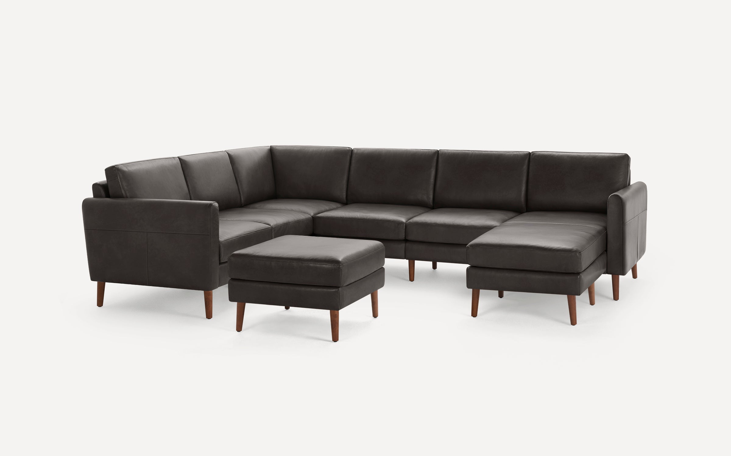 Dark gray leather sectional sofa with wooden legs and a matching ottoman on a white background.