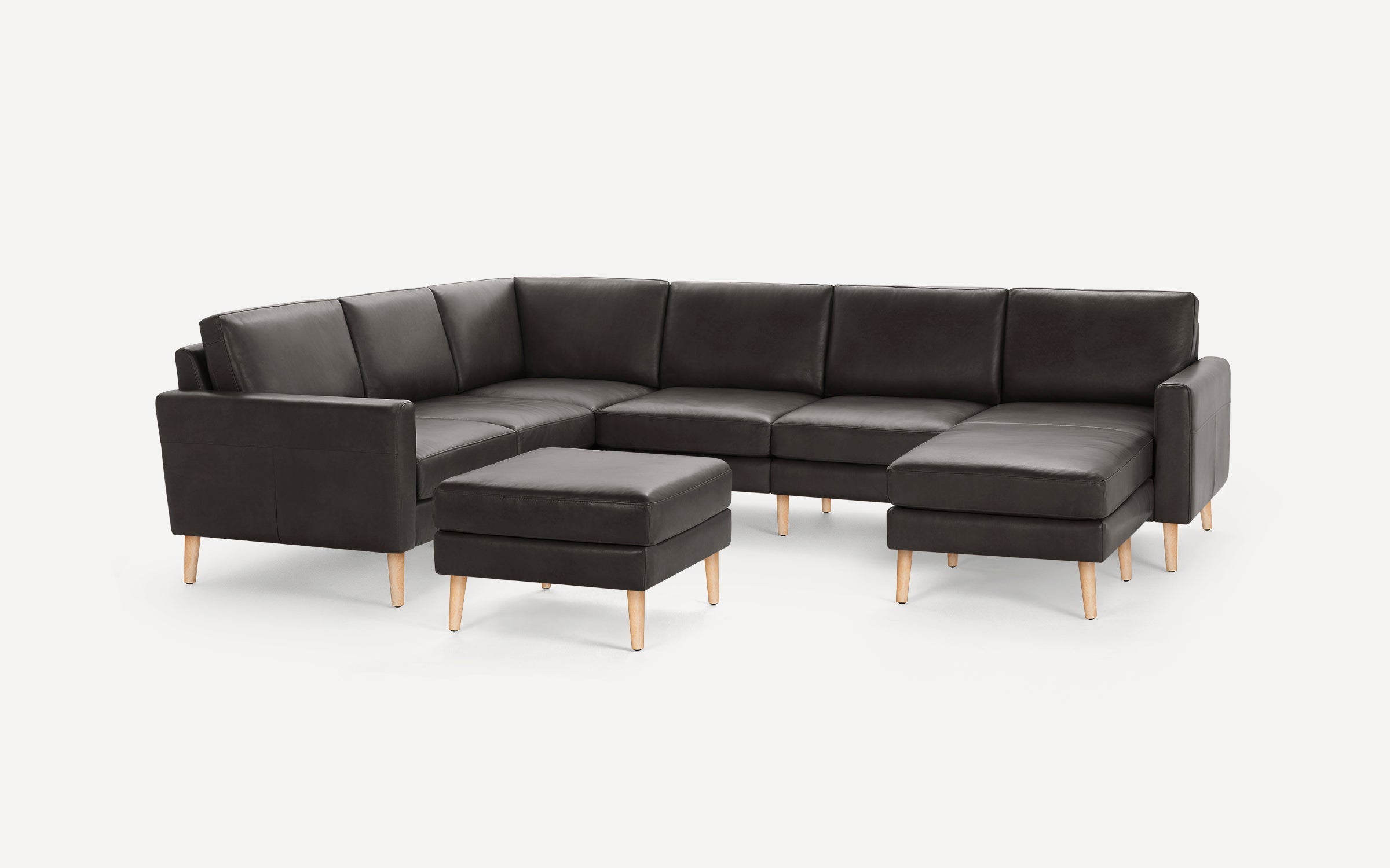 Dark gray modern sectional sofa with wooden legs and matching ottoman on plain white background.