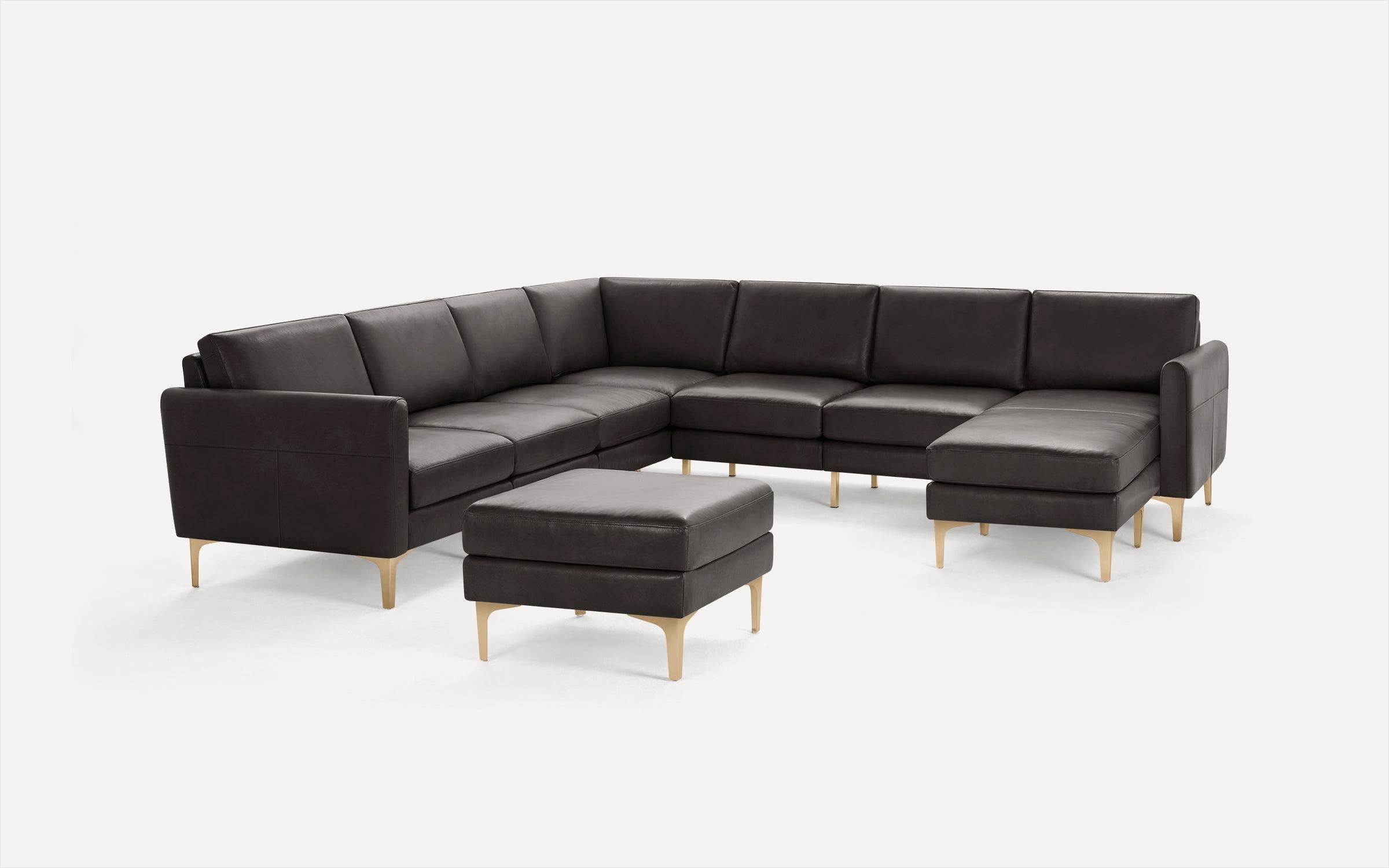 Modern dark gray sectional leather sofa with matching ottoman and light wooden legs on white background.