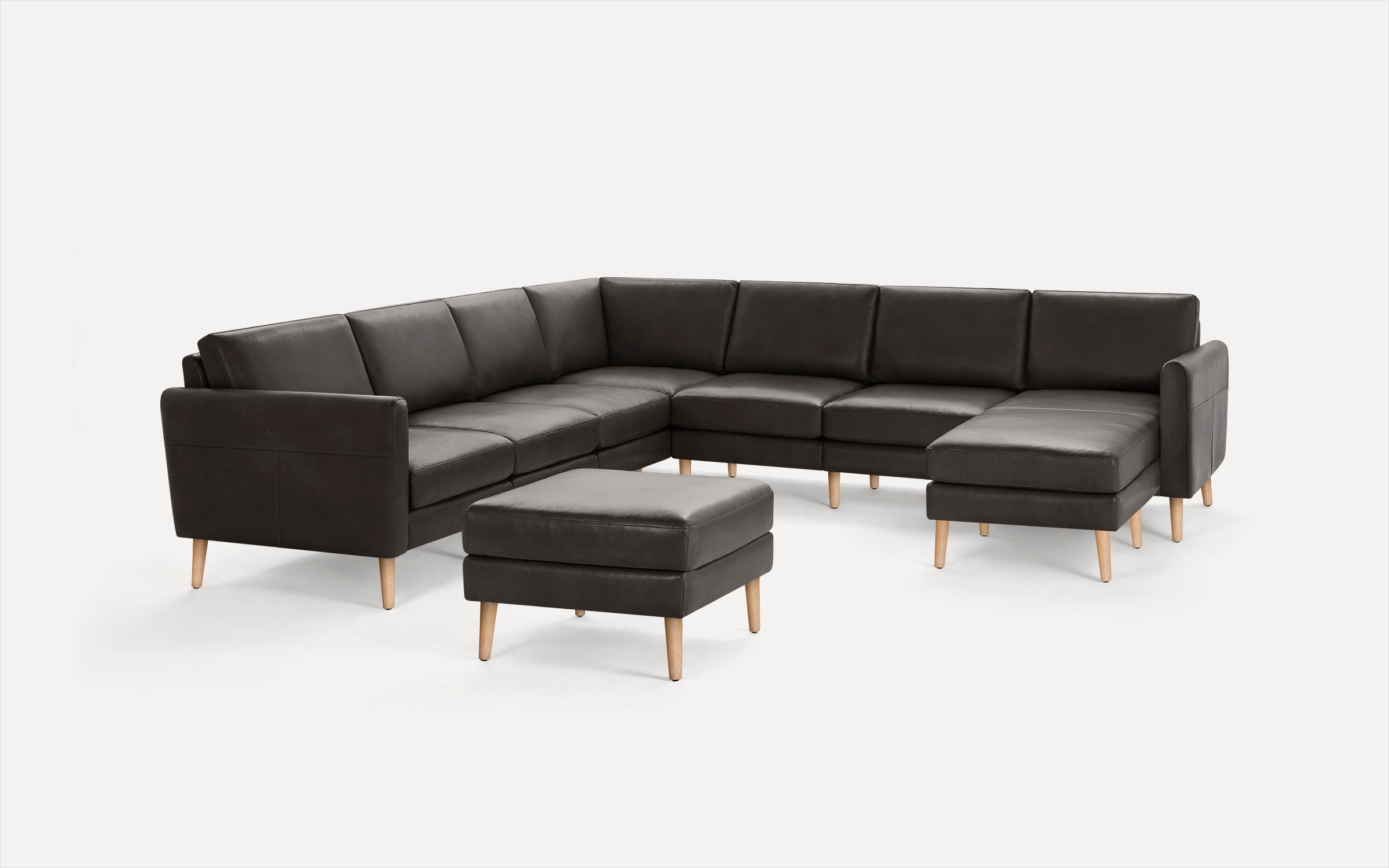 Dark gray leather sectional sofa with wooden legs and matching ottoman, modern and minimalist design.