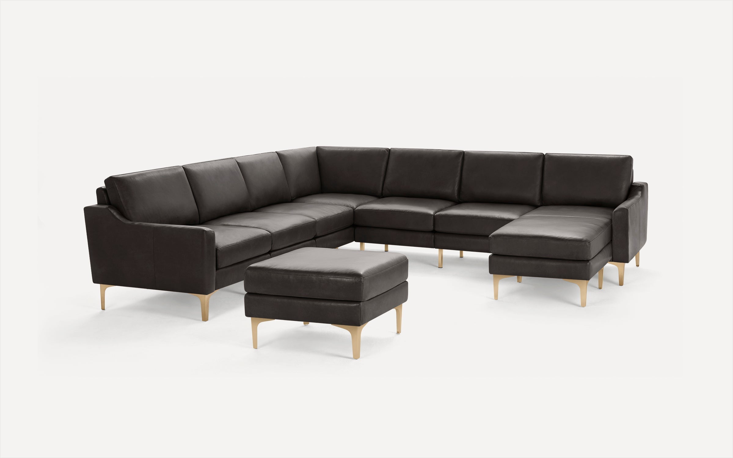 Modern dark gray leather sectional sofa with matching ottoman, featuring sleek light wooden legs and clean lines.