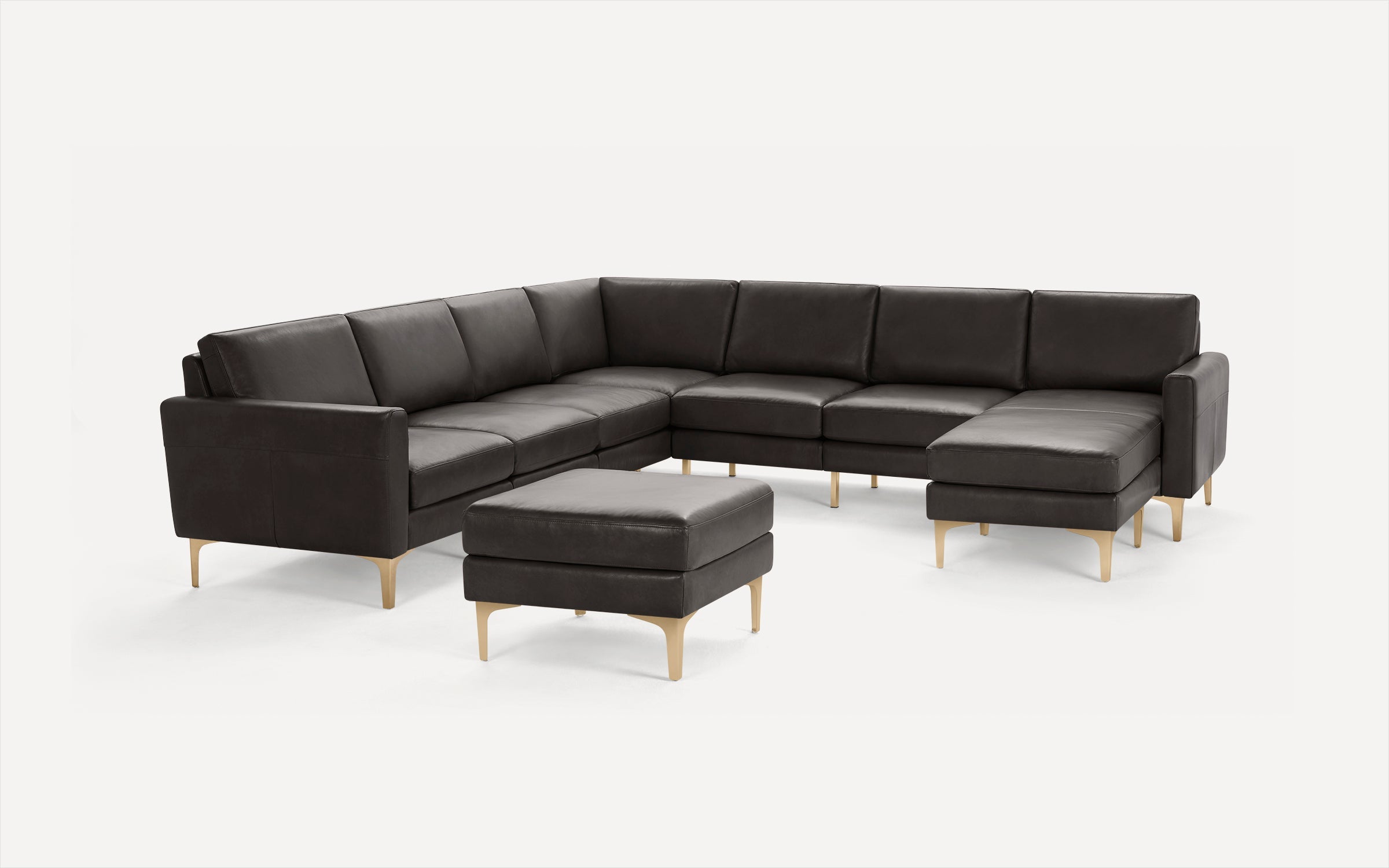 Modern dark brown leather sectional sofa with matching ottoman and light wooden legs on white background.