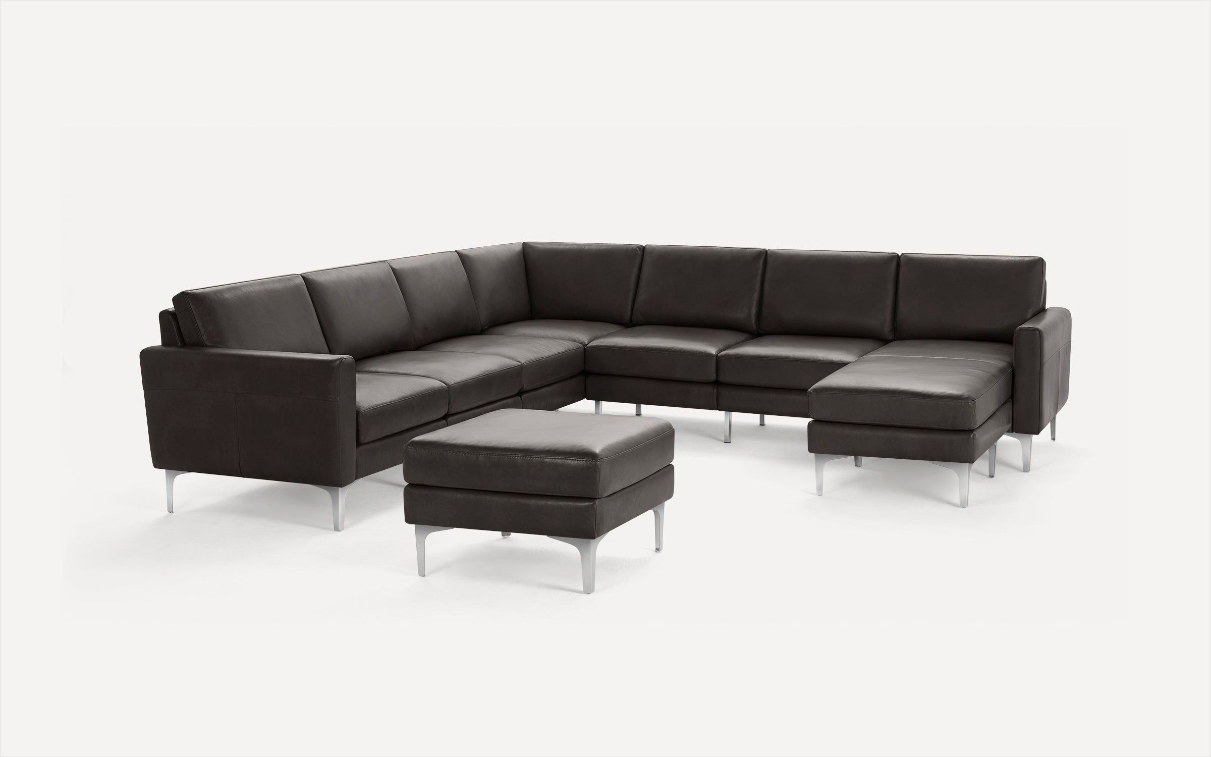 Modern dark gray leather sectional sofa with metal legs and matching ottoman on white background.