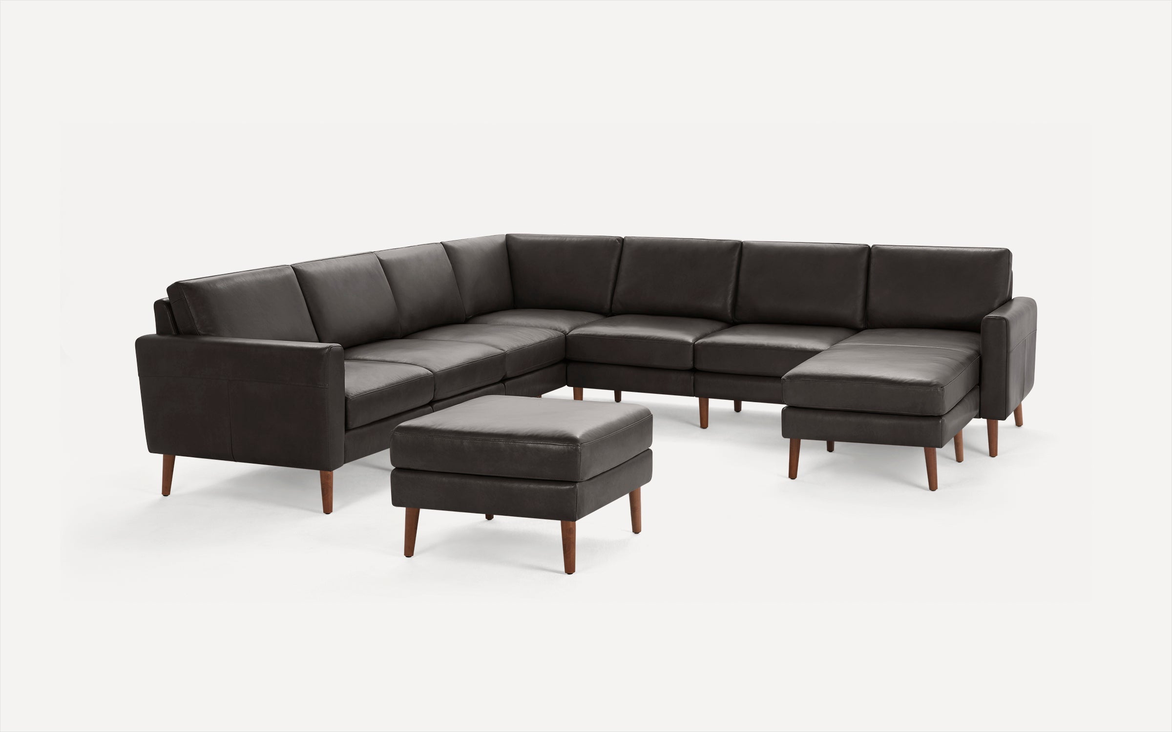 Dark brown leather sectional sofa with modern wooden legs and a matching ottoman on a white background.