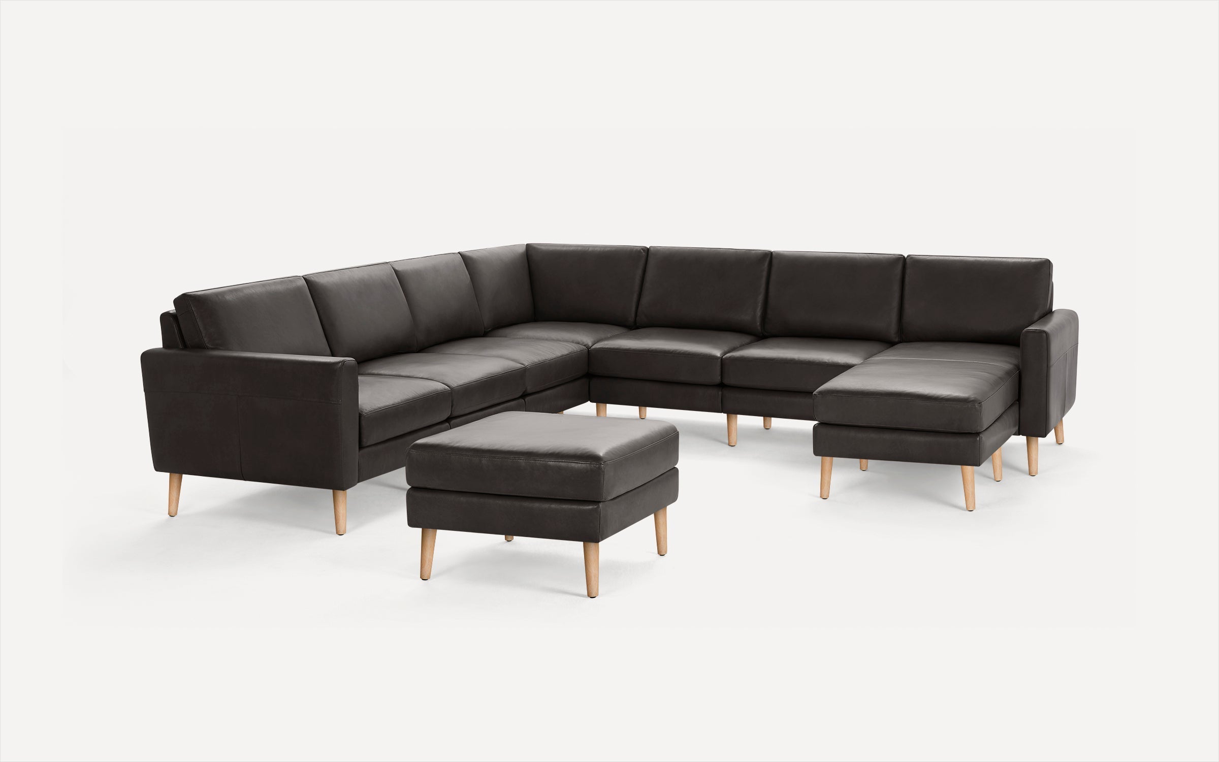 Large modern dark gray leather sectional sofa with chaise lounge and matching ottoman, light wooden legs, minimalist design.