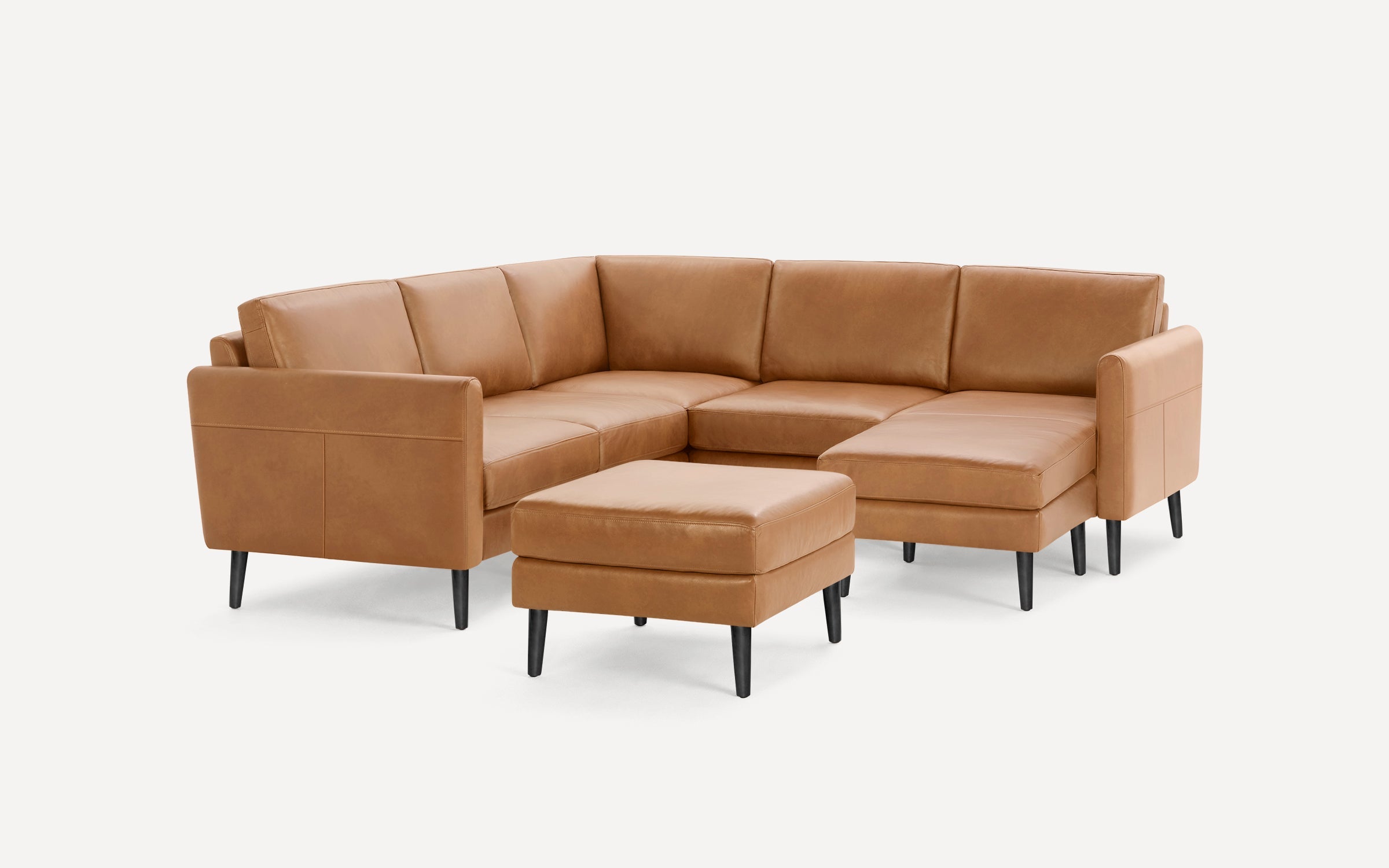 Modern L-shaped sectional sofa in tan leather with black tapered legs and matching ottoman on white background.