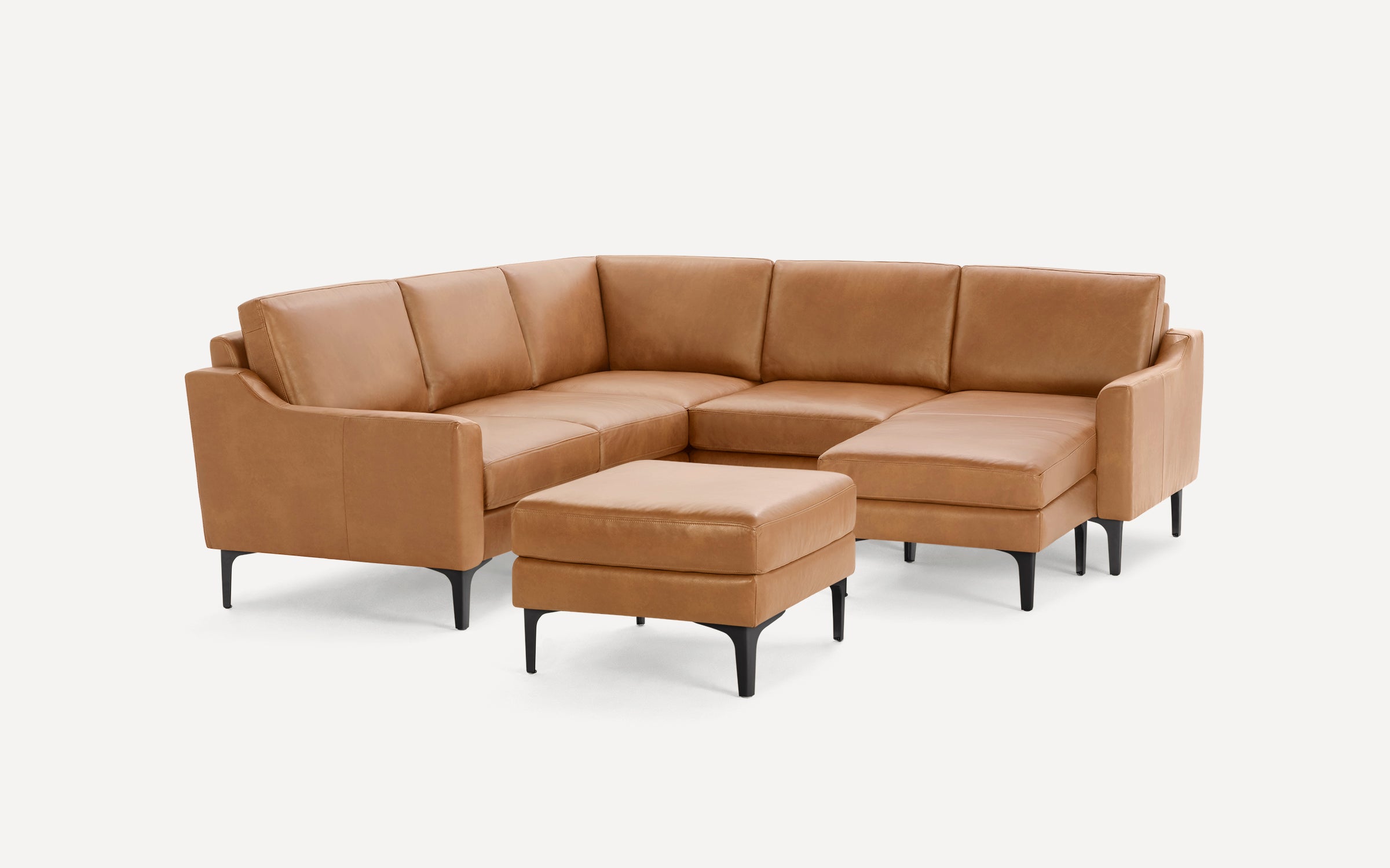 Modern tan leather L-shaped sectional sofa with black legs and matching ottoman on white background.