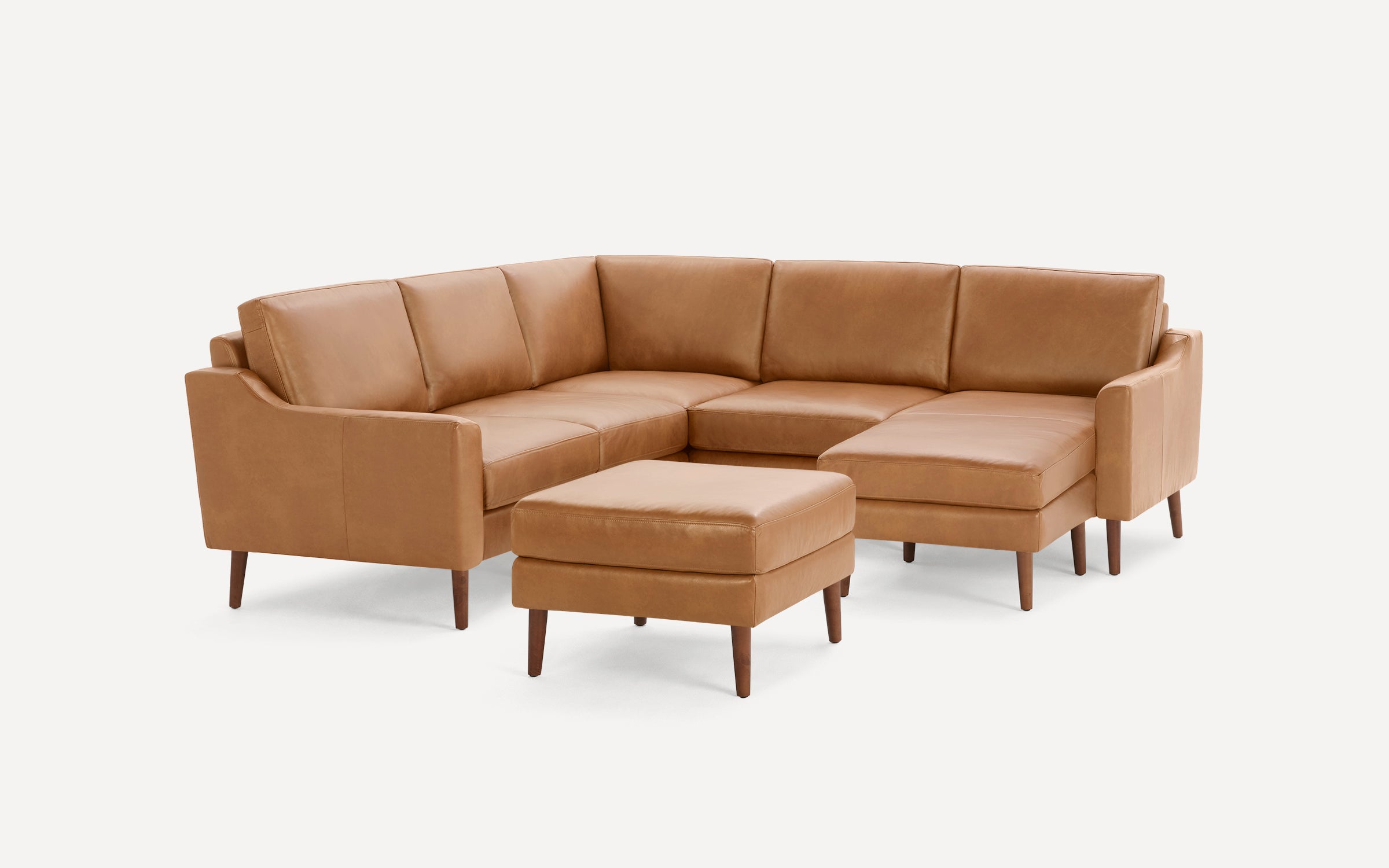 Tan leather L-shaped sectional sofa with clean lines, angled arms, wooden legs, and matching ottoman on white background.
