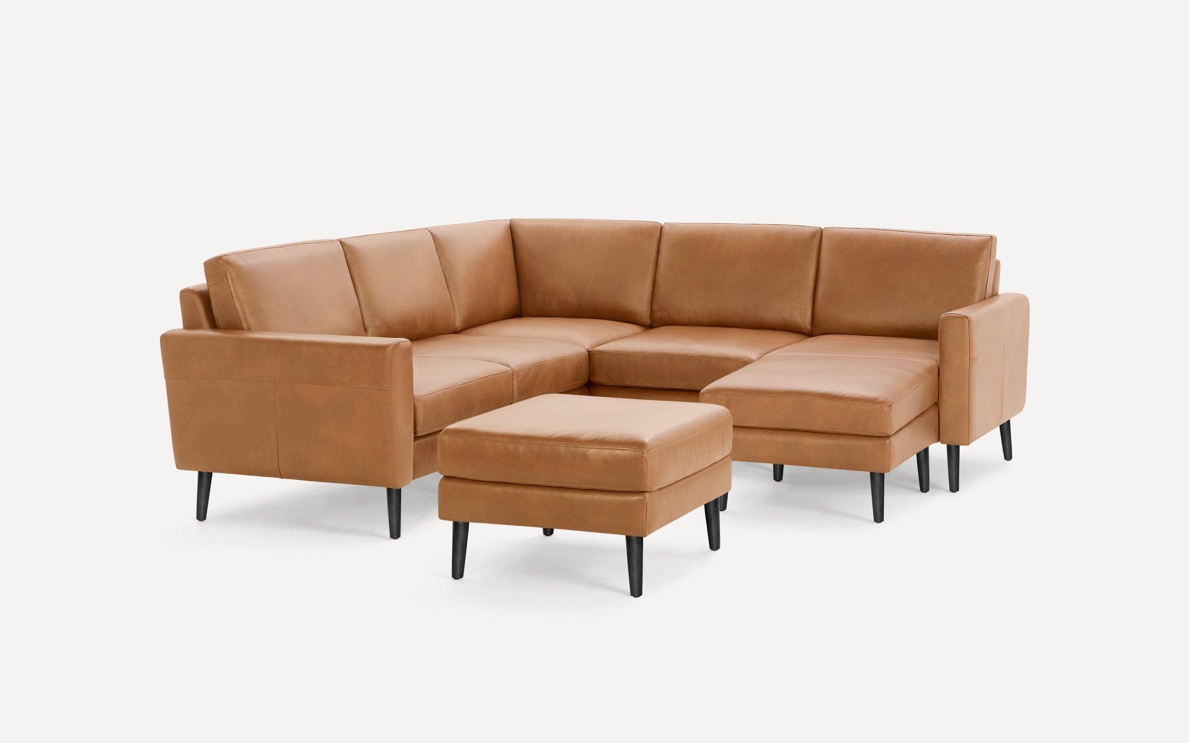 Tan leather sectional sofa with black legs, accompanied by a matching square ottoman on a white background.
