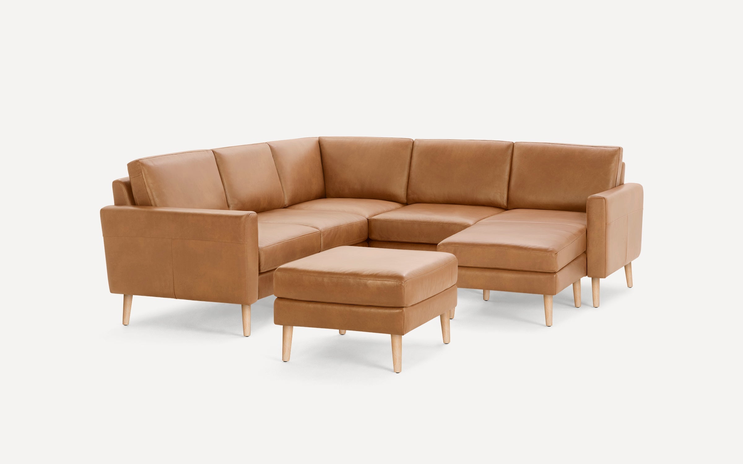 Modern tan leather sectional sofa with chaise lounge and matching ottoman, featuring light wood tapered legs and clean lines.