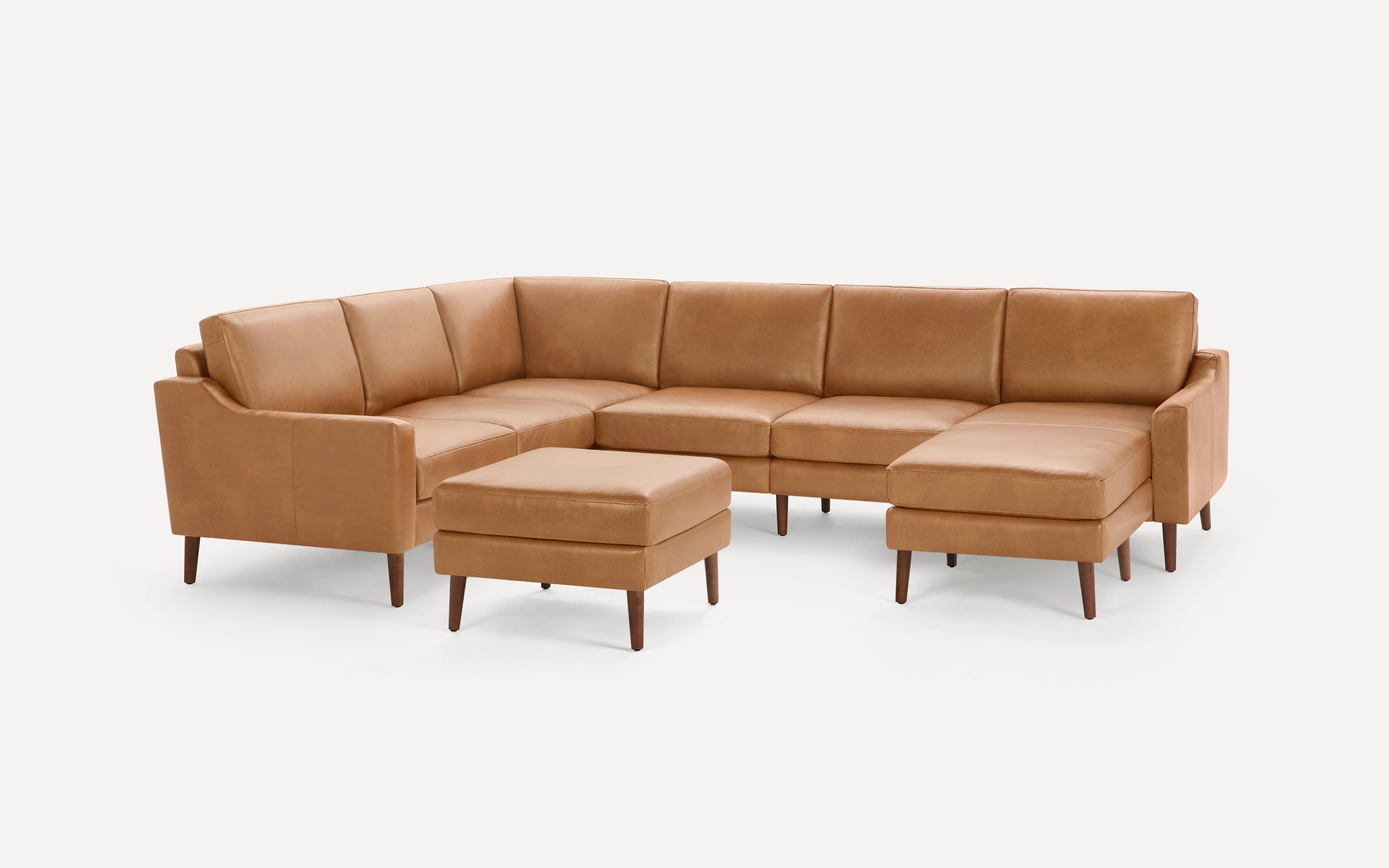 Modern tan leather sectional sofa with a matching ottoman, featuring clean lines and wooden legs on a white background.