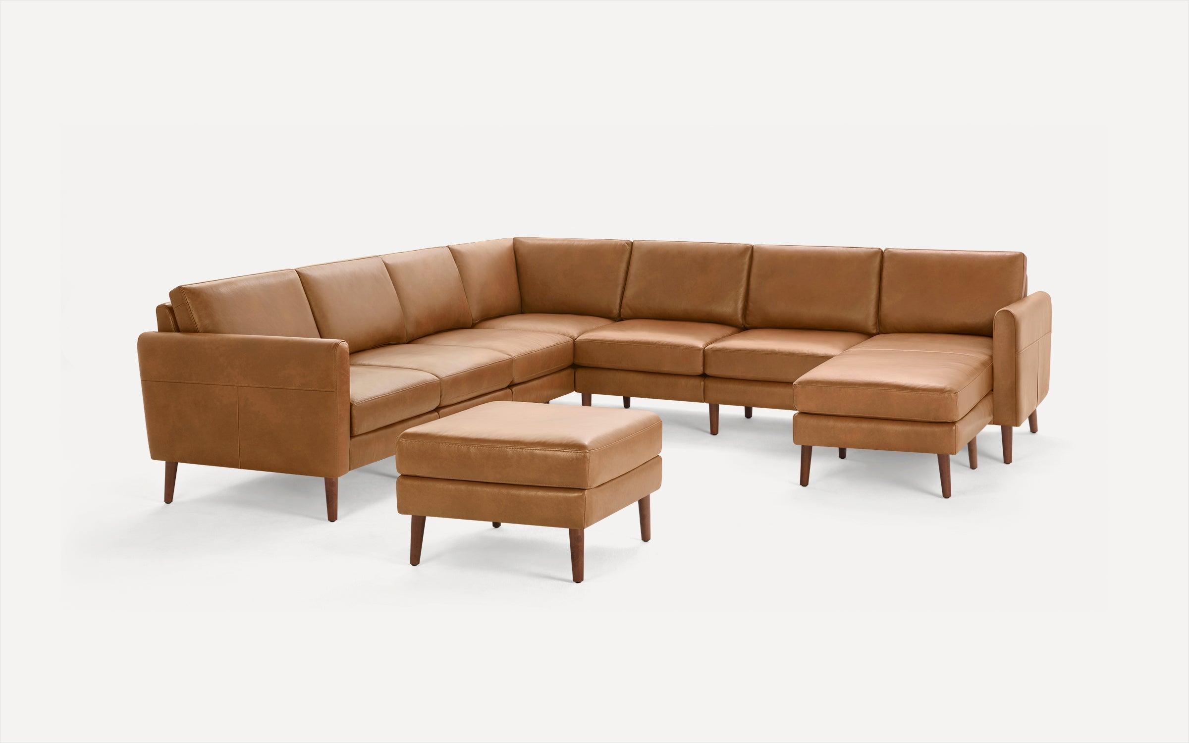 Mid-century modern tan leather sectional sofa with clean lines and matching ottoman on wooden legs.