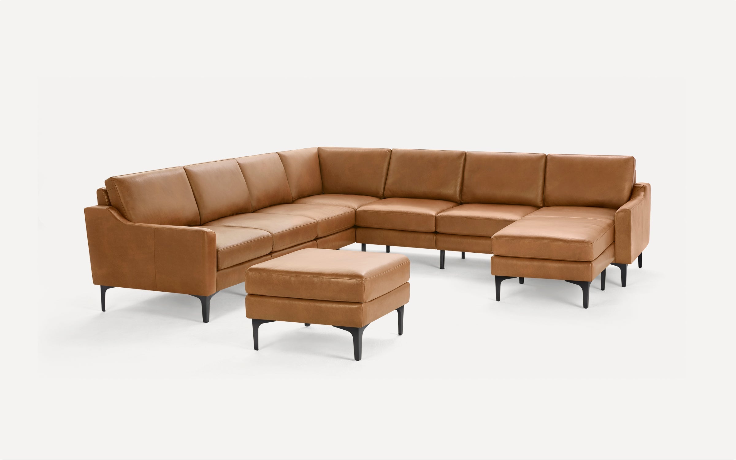 Modern tan leather sectional sofa with black legs and matching ottoman, set against a plain white background.