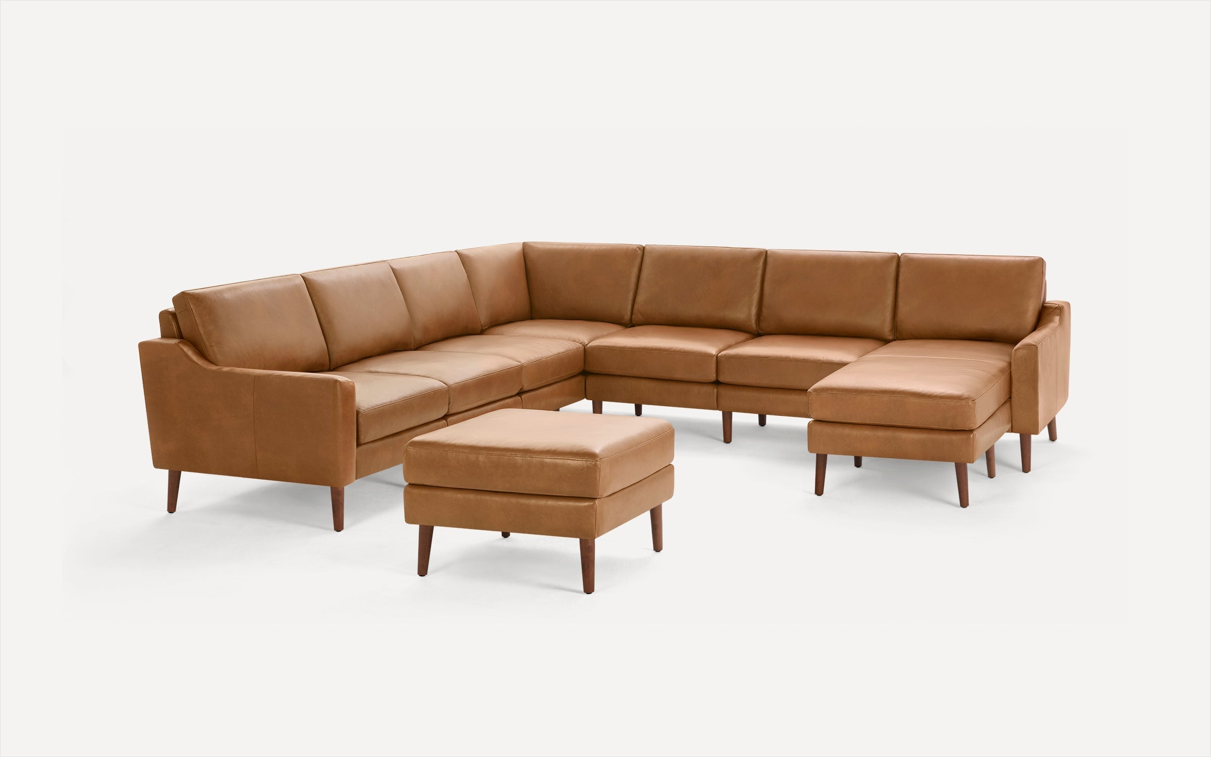 Mid-century modern L-shaped sectional sofa and ottoman in tan leather with wooden legs on white background.