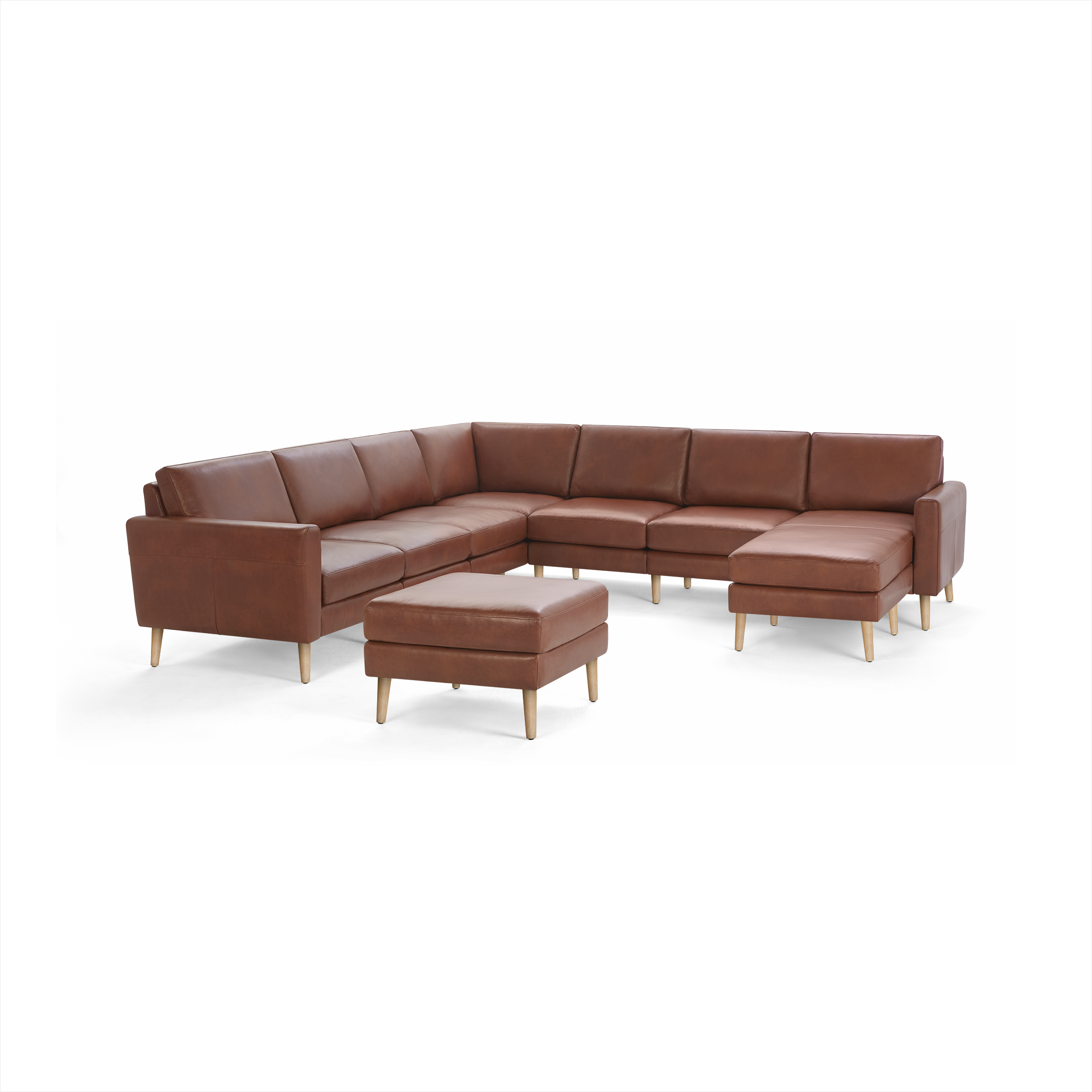 Large L-shaped brown leather sectional sofa with wooden legs and matching ottoman on a black background.