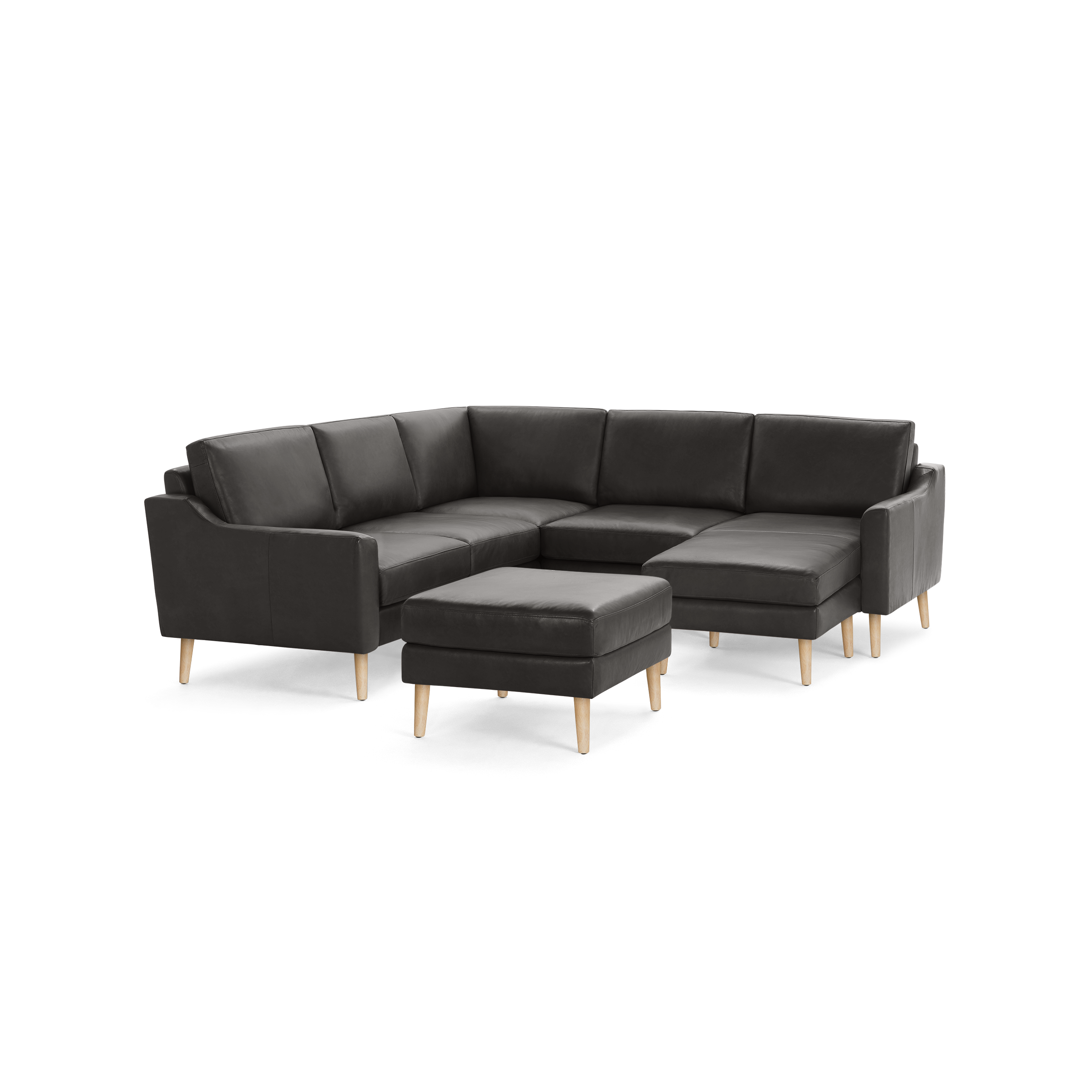 Dark gray leather L-shaped sectional sofa with wooden legs and matching ottoman on black background.