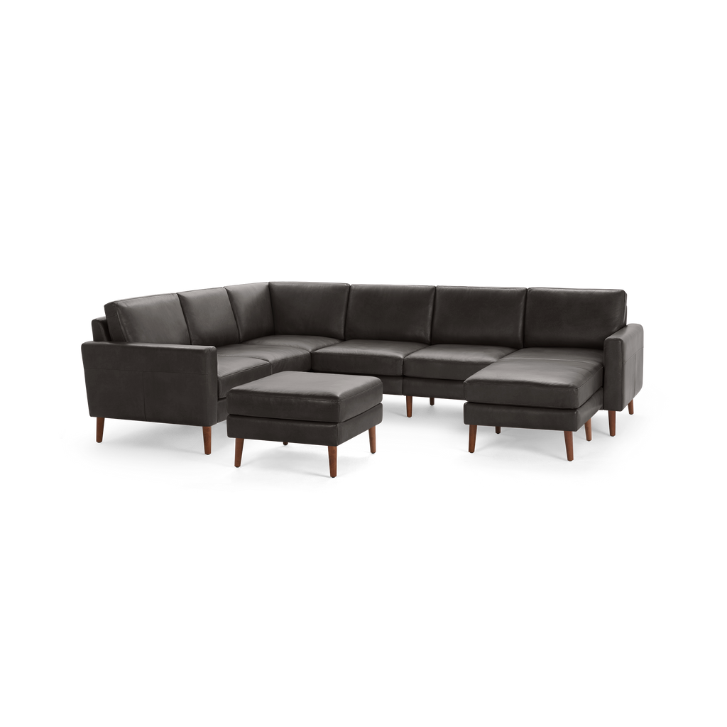 Dark gray leather sectional sofa with wooden legs and matching ottoman, featuring clean lines and modern design.
