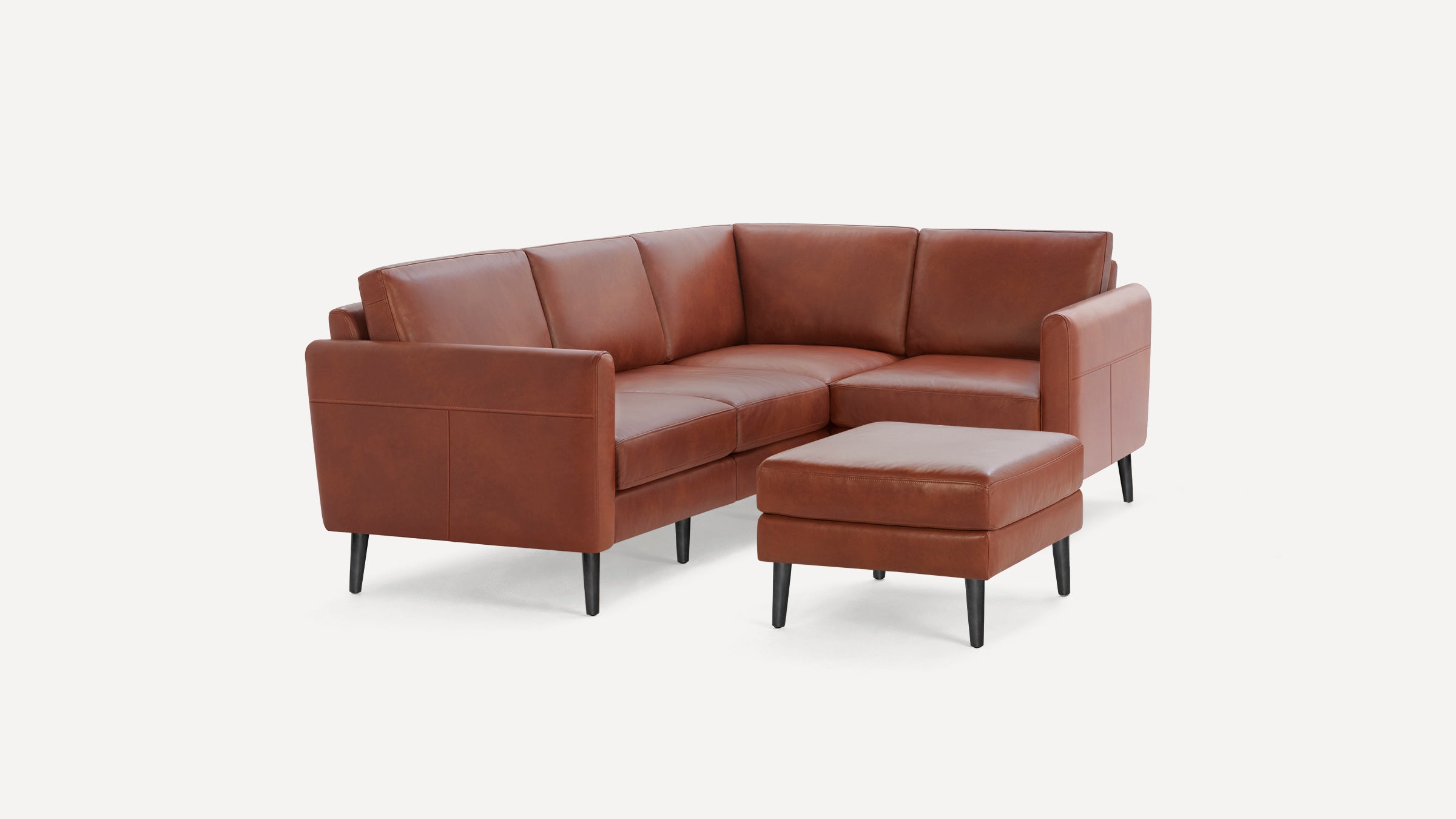 Brown leather L-shaped sectional sofa with black tapered legs and matching ottoman on white background.