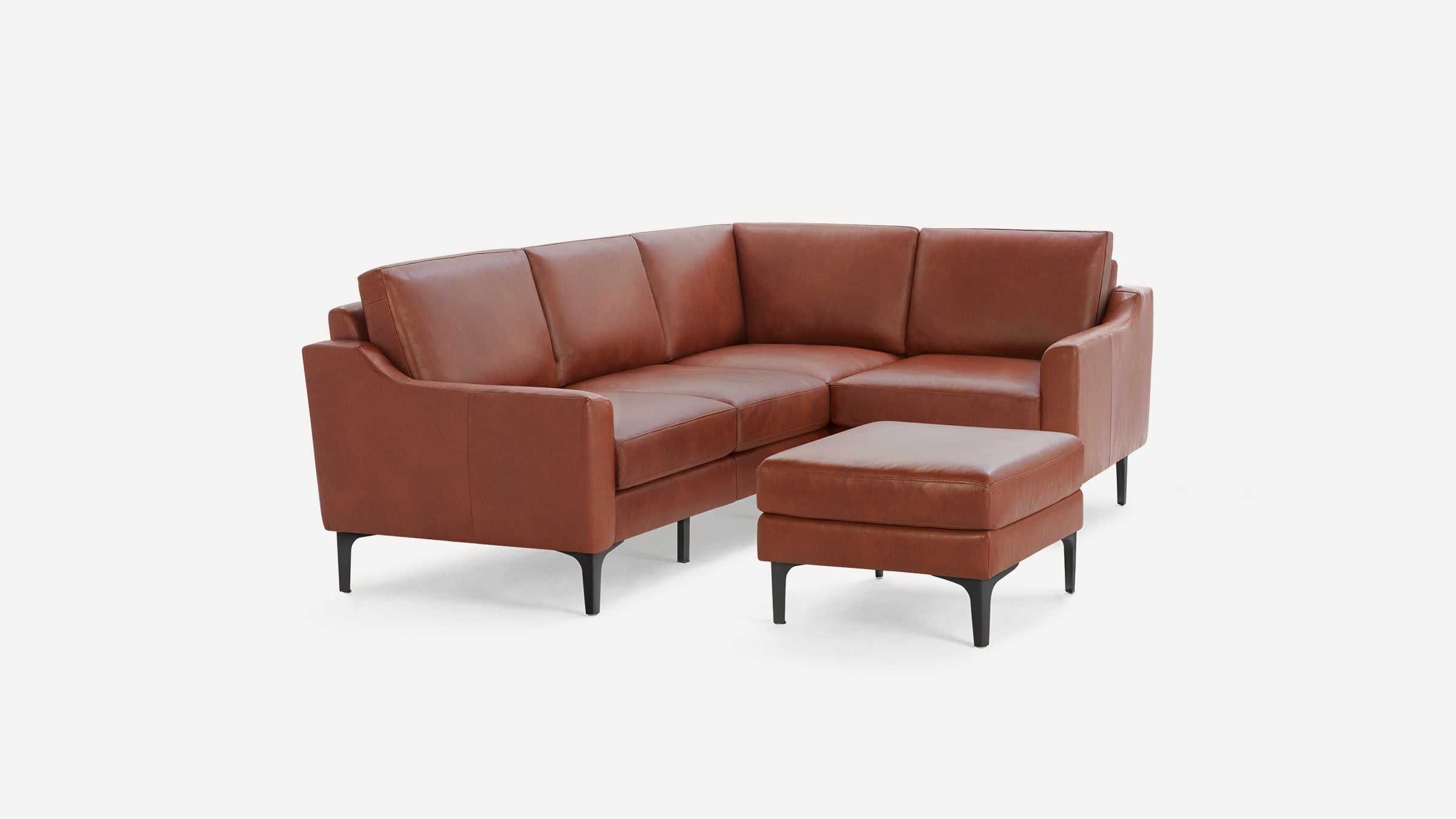 Brown leather L-shaped sectional sofa with matching ottoman, straight arms, and black tapered legs on white background.