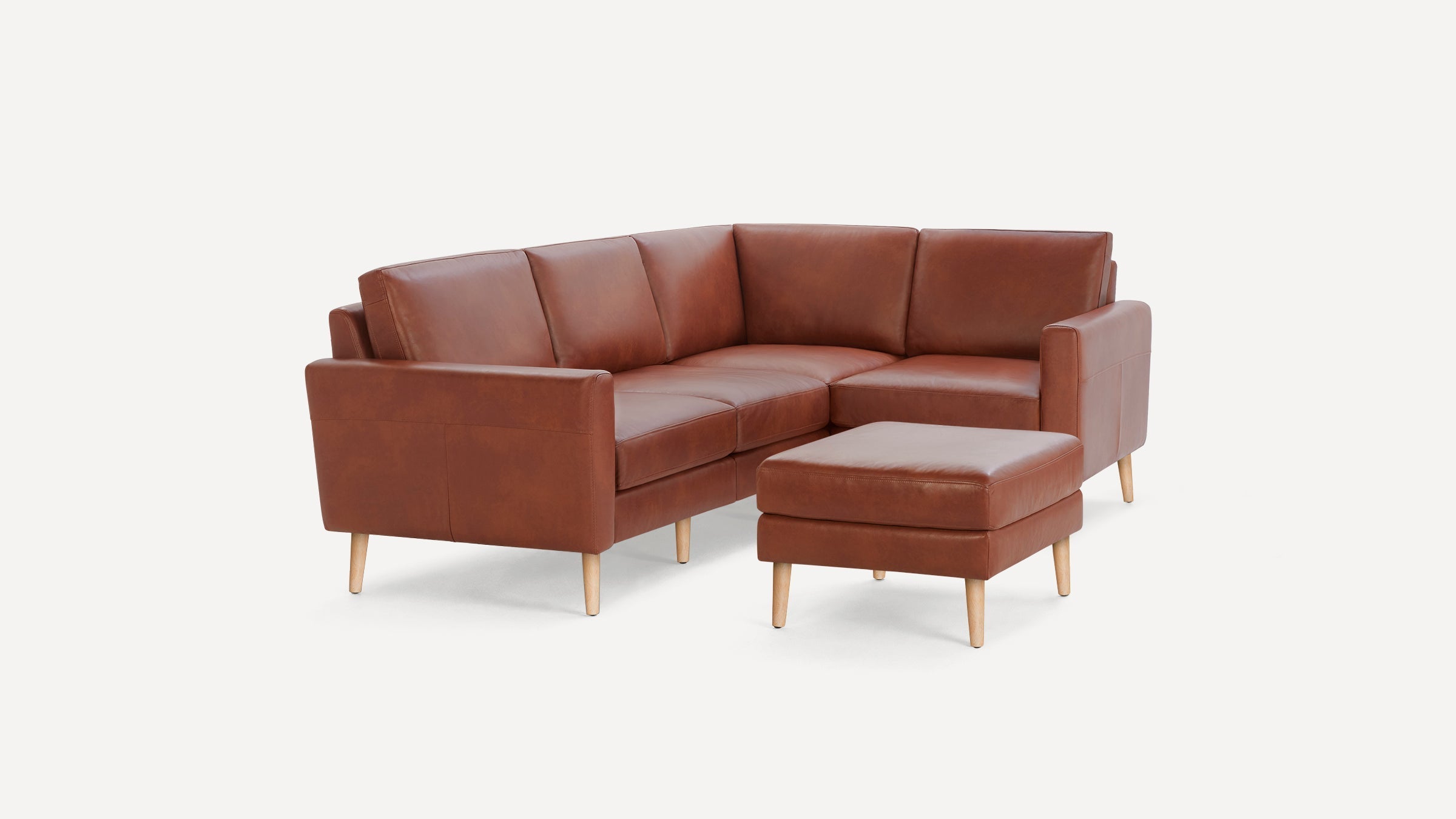 Brown leather L-shaped sectional sofa with matching ottoman and light wooden legs on white background.