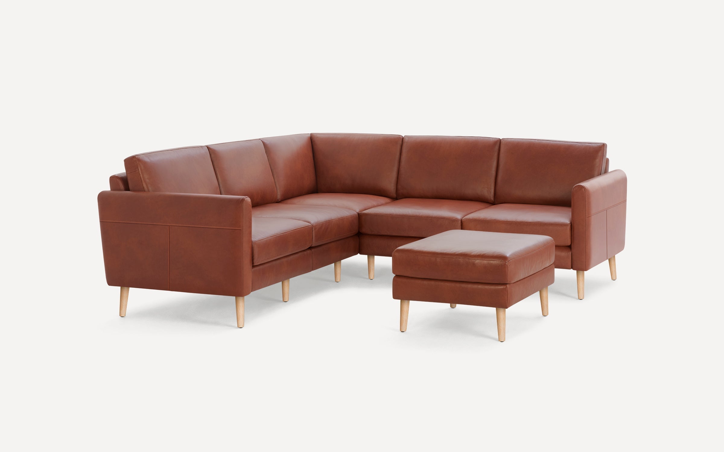 Mid-century style brown leather sectional sofa with wooden legs and matching ottoman, set against a plain white background.