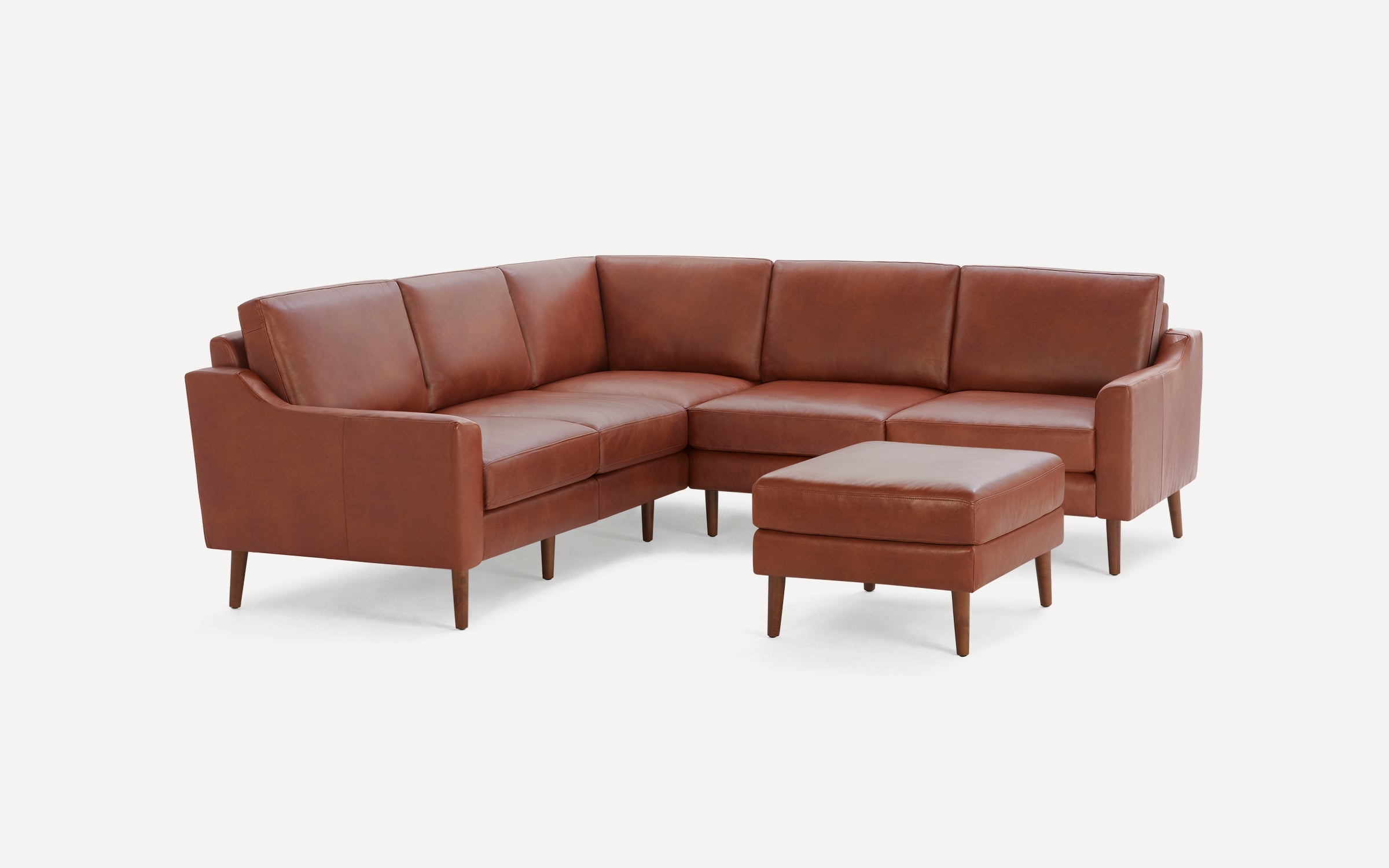 Brown leather sectional sofa with wooden tapered legs and matching ottoman on white background.