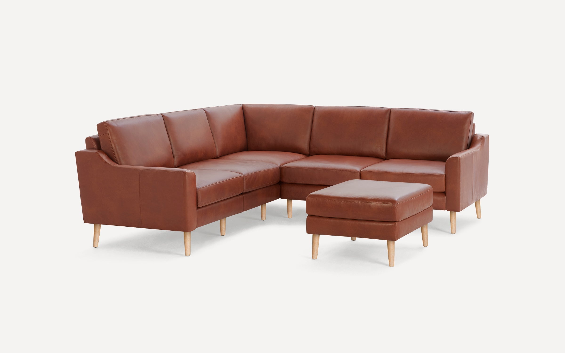 Modern brown leather L-shaped sectional sofa with matching ottoman and light wooden legs on white background.