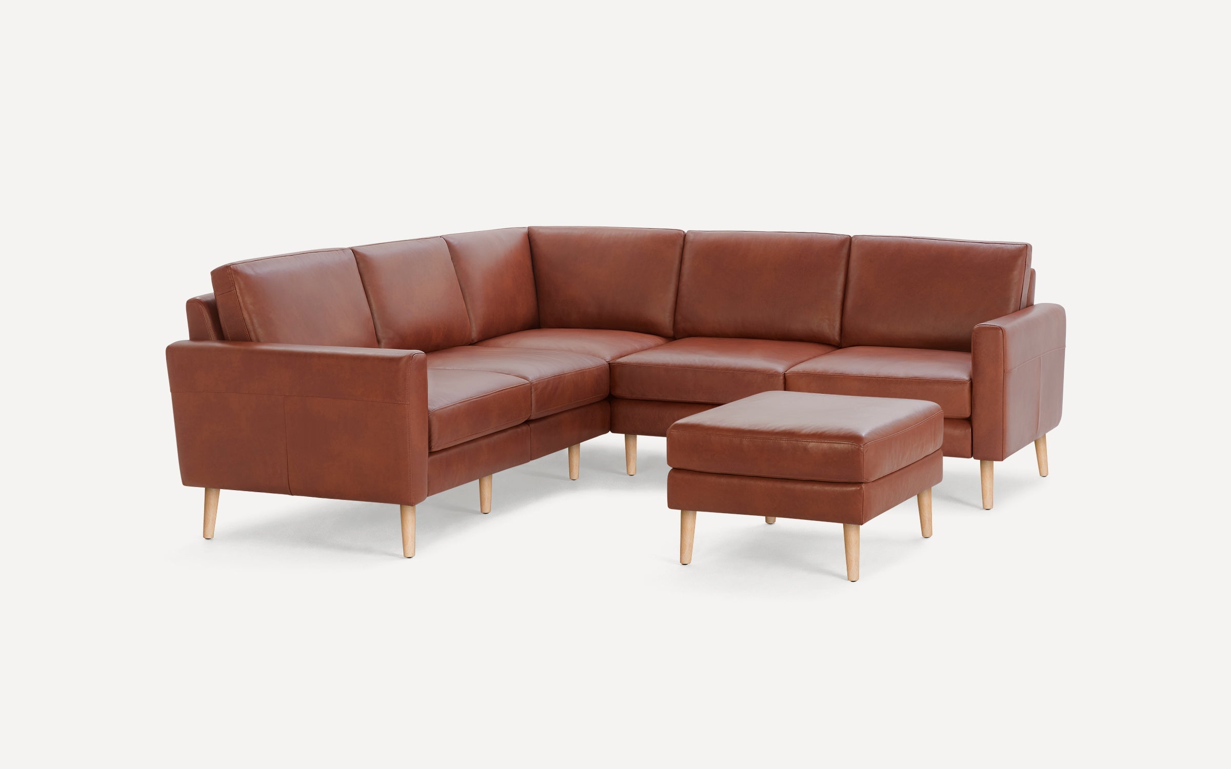 Brown leather mid-century modern sectional sofa with clean lines and light wooden legs, accompanied by matching ottoman.
