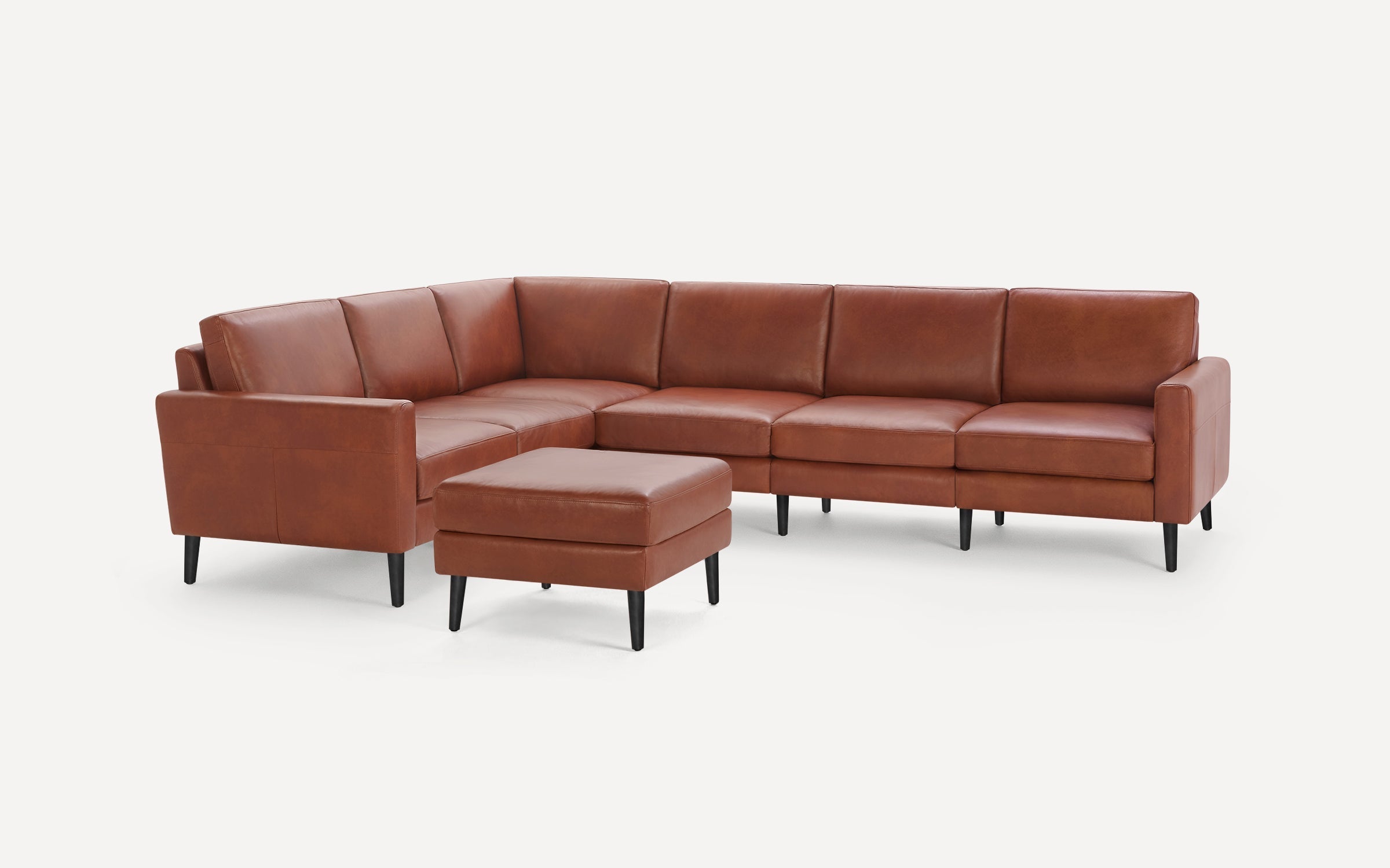 Brown leather sectional sofa with clean lines, black tapered legs, and matching ottoman, set against a white background.