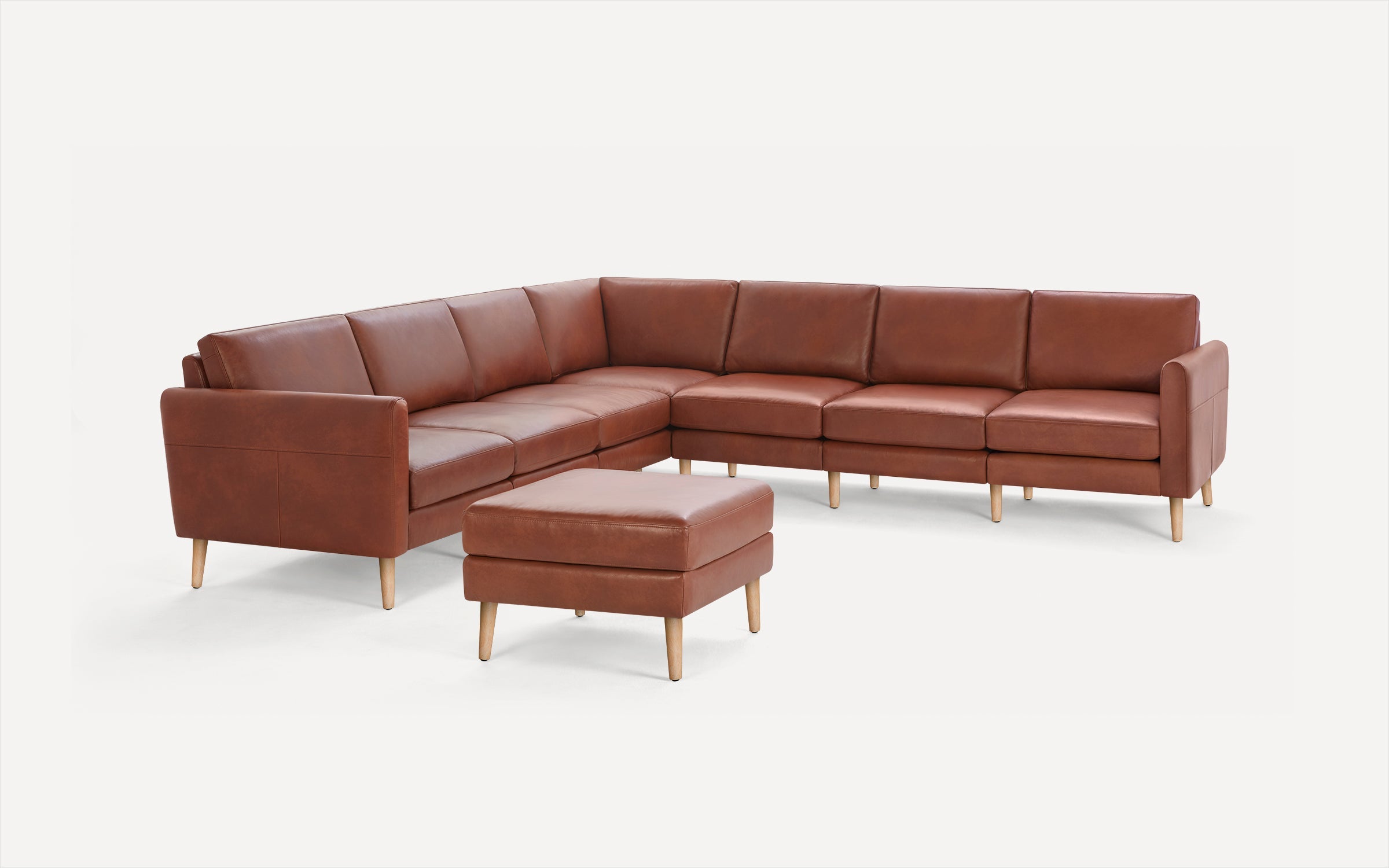 Brown leather L-shaped sectional sofa with matching ottoman, wooden legs, and clean, modern design.