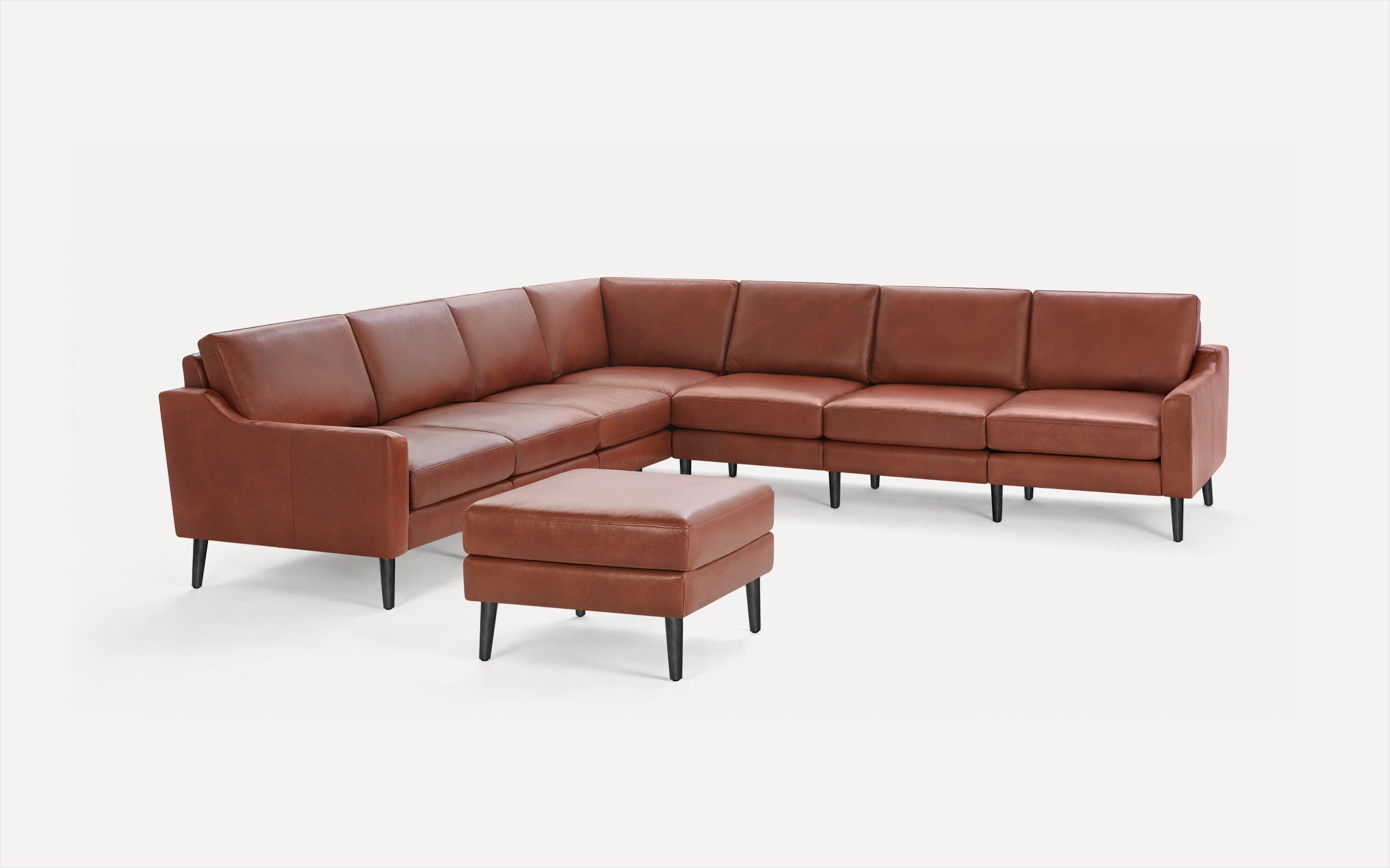 Large L-shaped brown leather sectional sofa with black wooden legs and matching ottoman against white background.