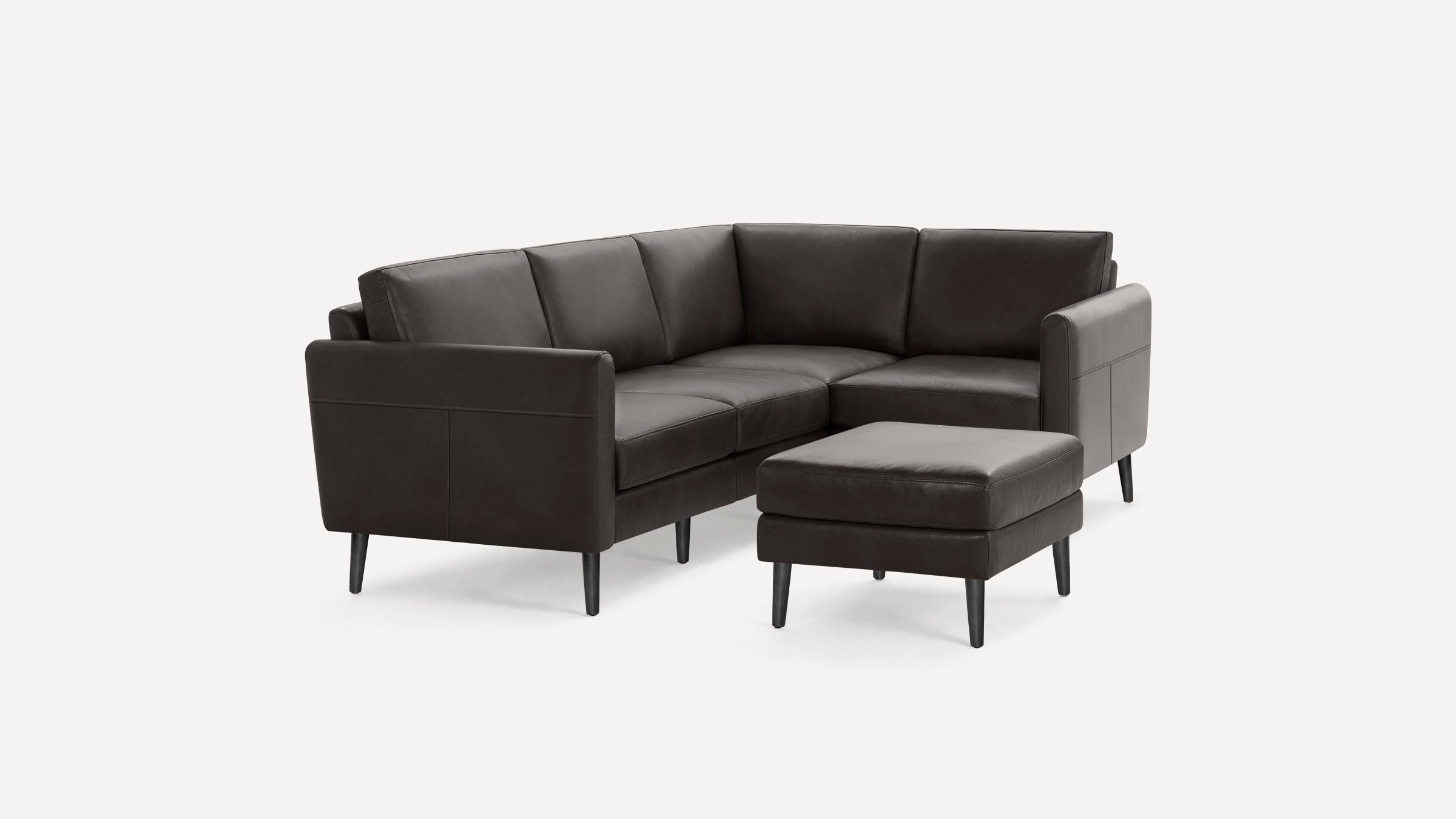 Dark gray leather sectional sofa with clean lines and matching ottoman, set on slim black legs, modern design.