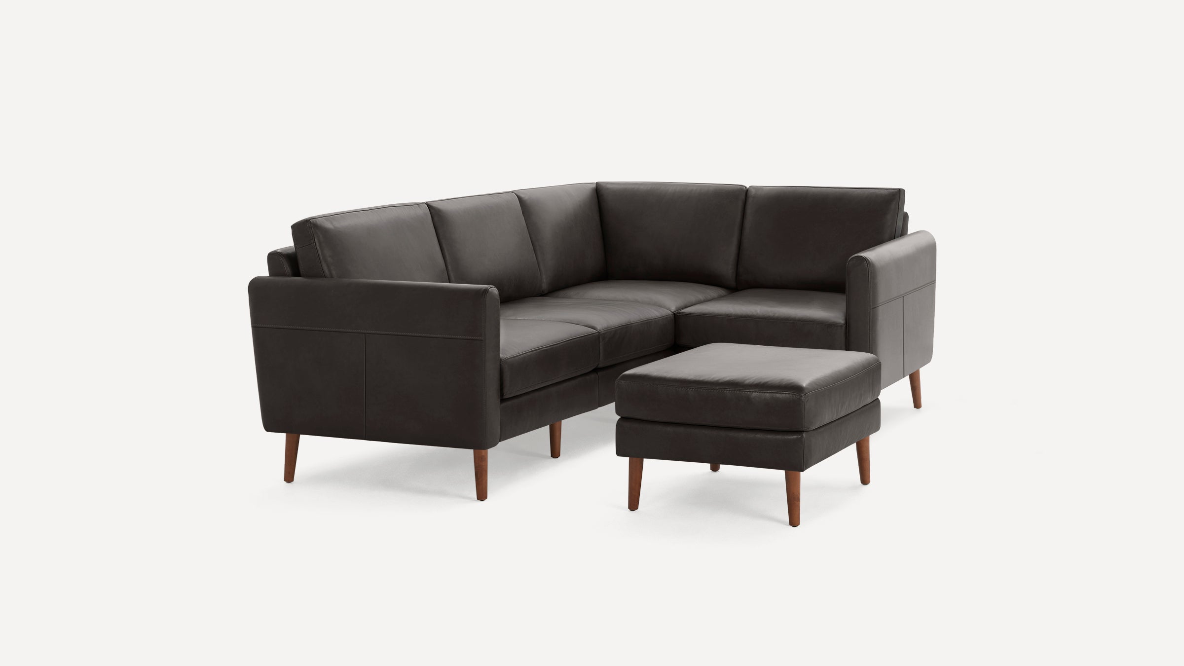 Dark gray leather sectional sofa with wooden legs and matching ottoman, minimalist modern design on white background.
