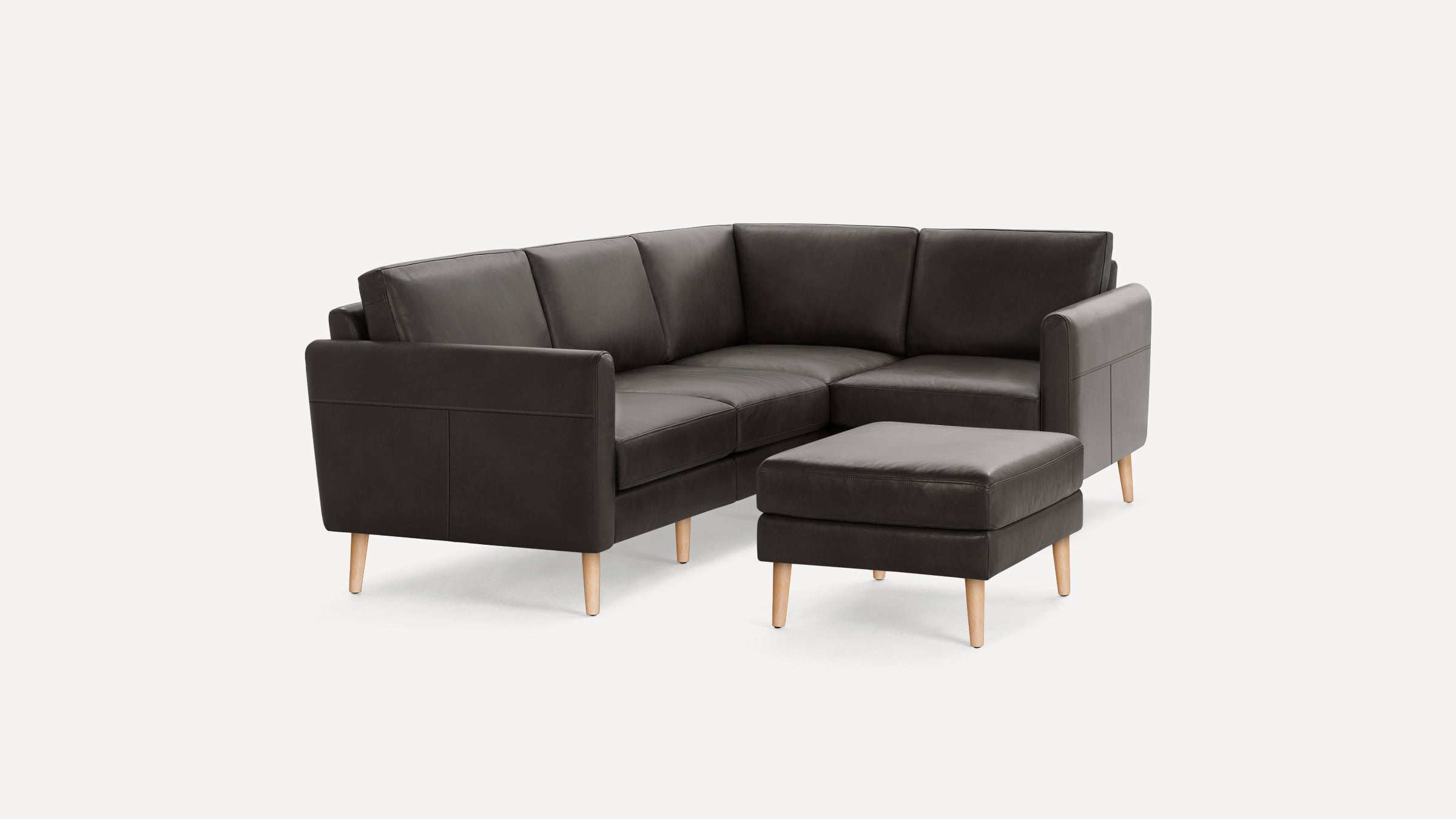 Dark gray leather sectional sofa with wooden legs and matching ottoman, minimalist mid-century modern design.