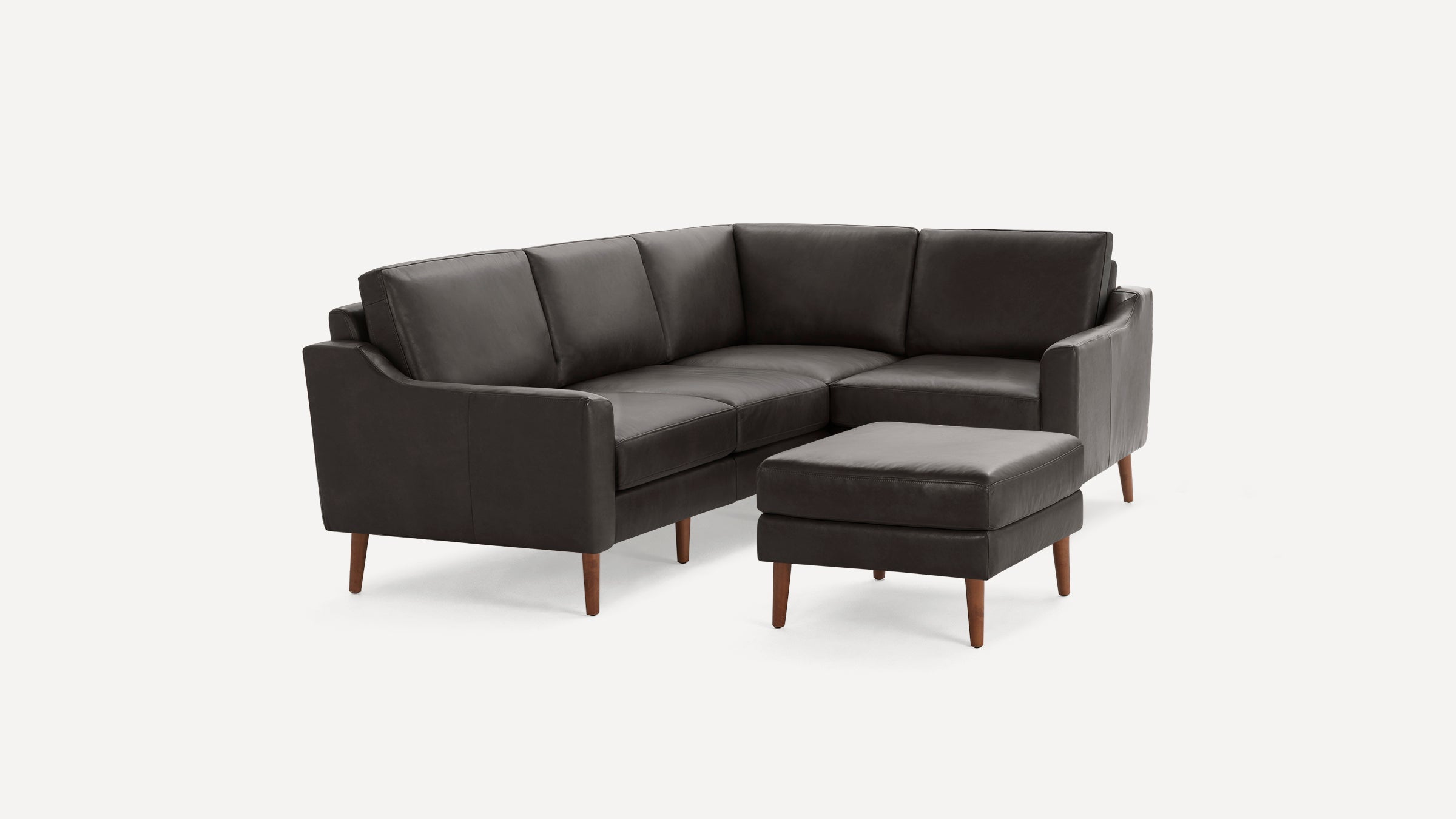 Dark gray leather sectional sofa with wooden legs and a matching ottoman, modern and minimalist design.