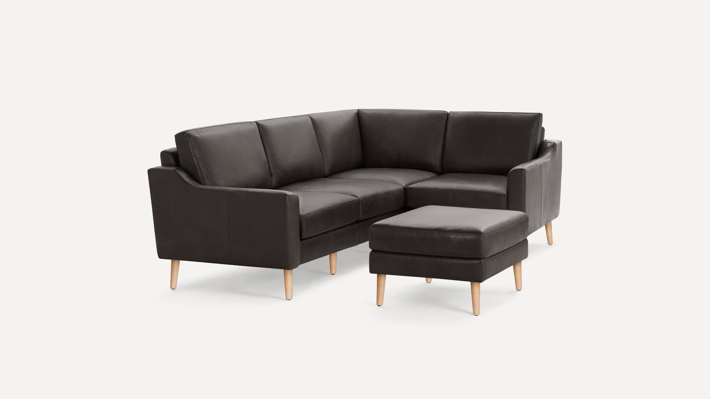 Dark gray modern leather sectional sofa with wooden legs and a matching ottoman on a white background.