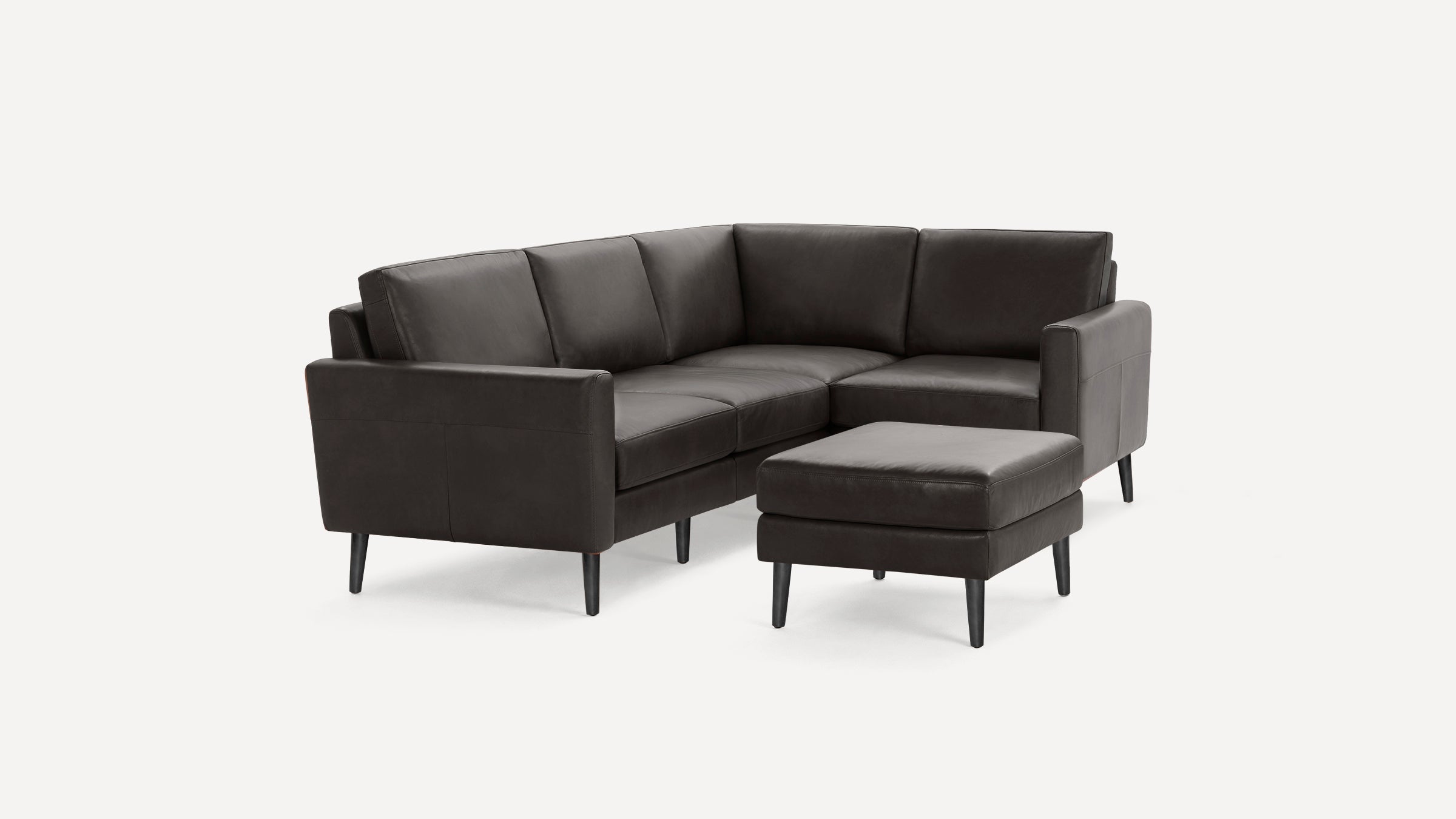Dark brown leather L-shaped sectional sofa with matching ottoman and tapered black wooden legs on white background.