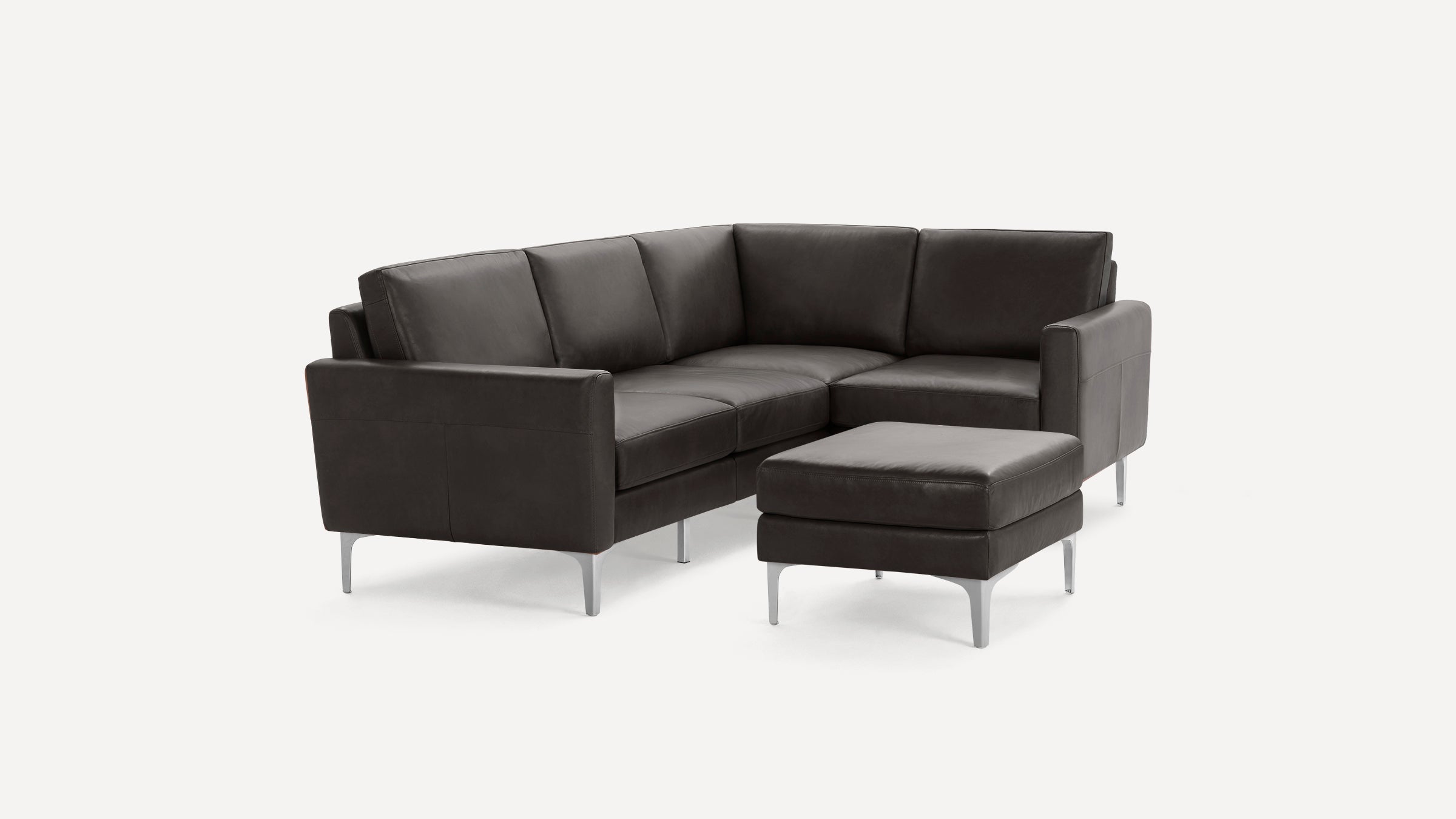 Modern dark gray leather L-shaped sofa with metal legs and matching ottoman on white background.