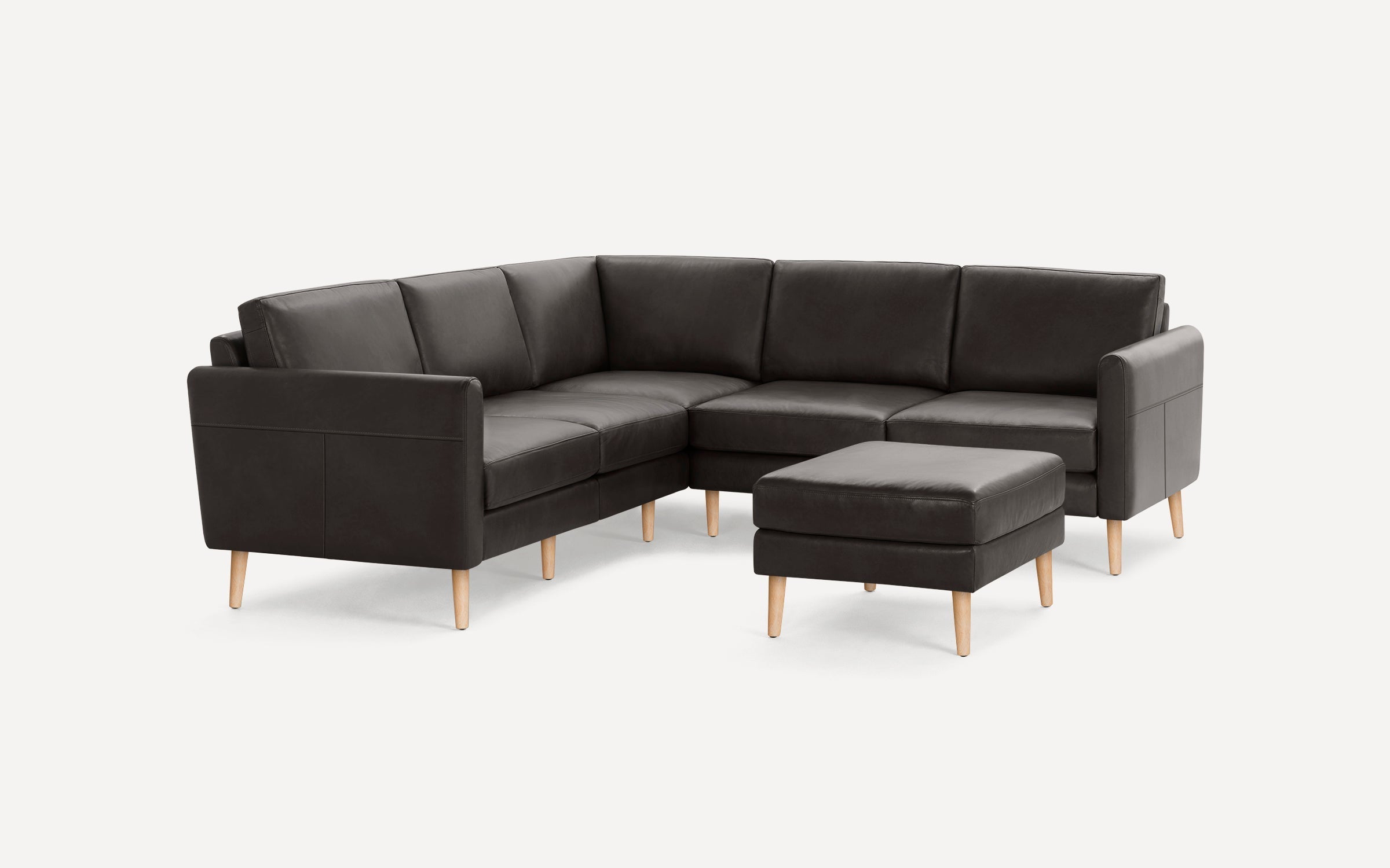Dark gray sectional sofa with light wooden legs, featuring a matching ottoman, set against a plain white background.