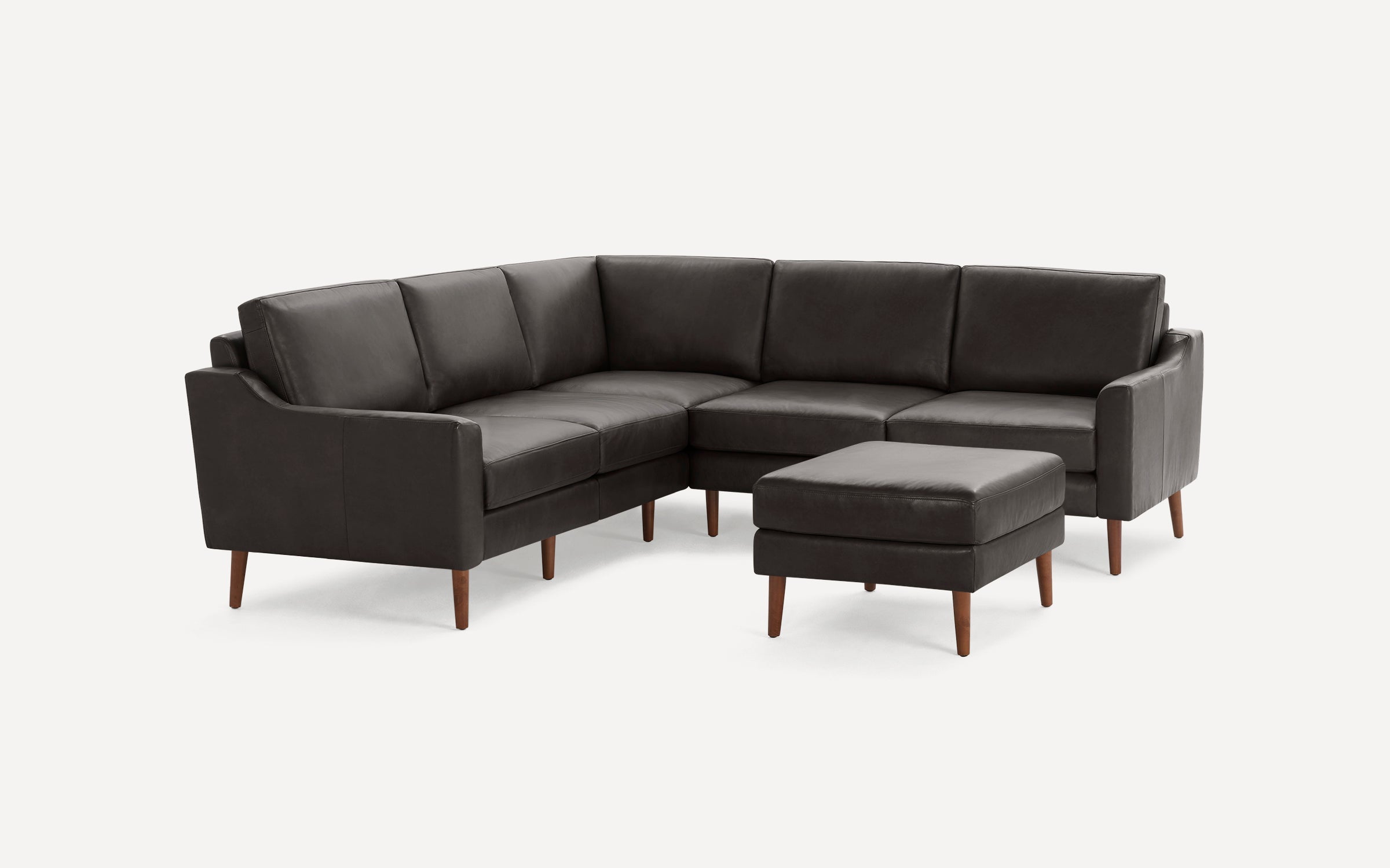 Dark grey leather L-shaped sectional sofa with matching ottoman, supported by slender wooden legs.