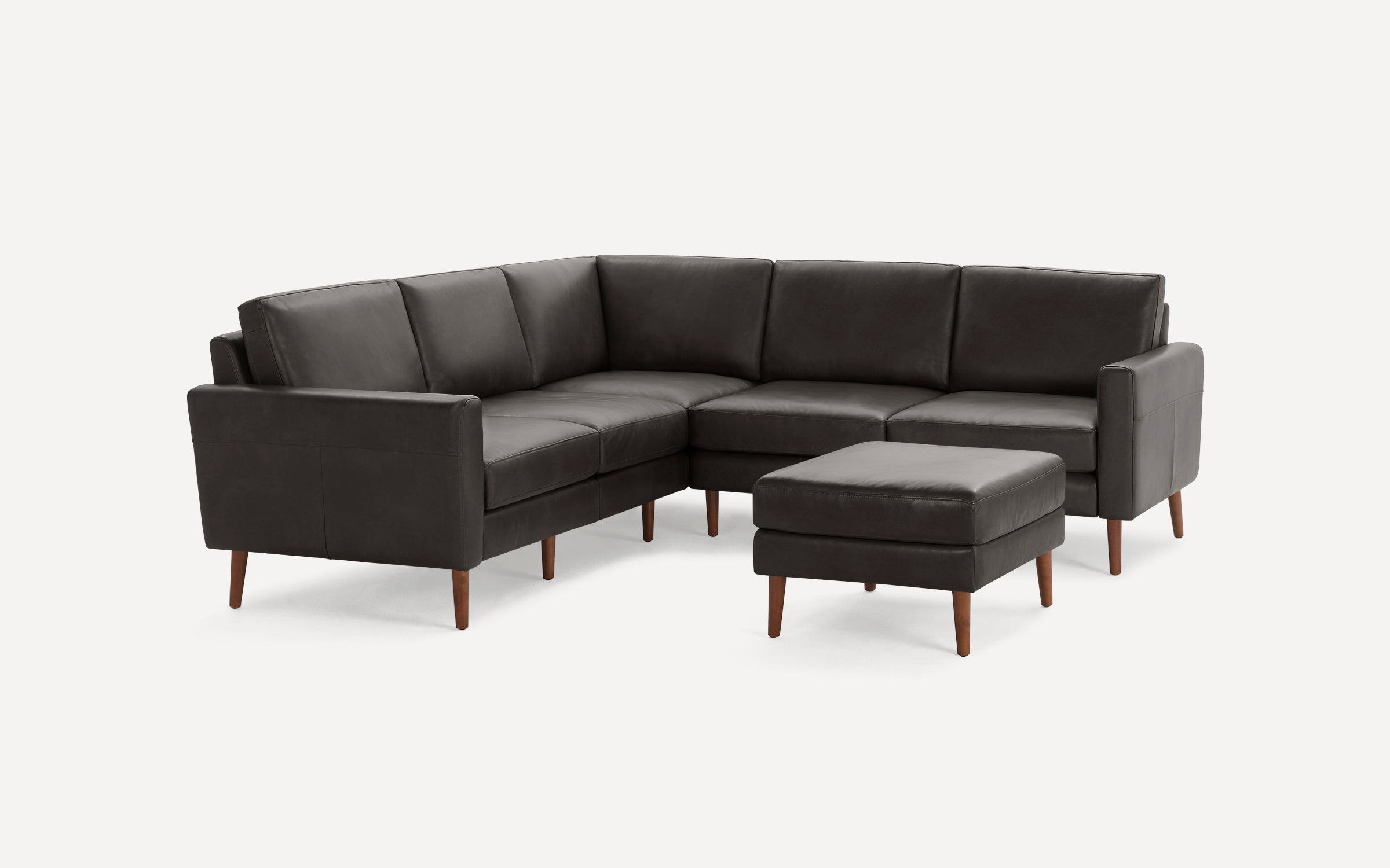 Dark gray leather L-shaped sectional sofa with wooden legs and matching padded ottoman, minimalist modern design.