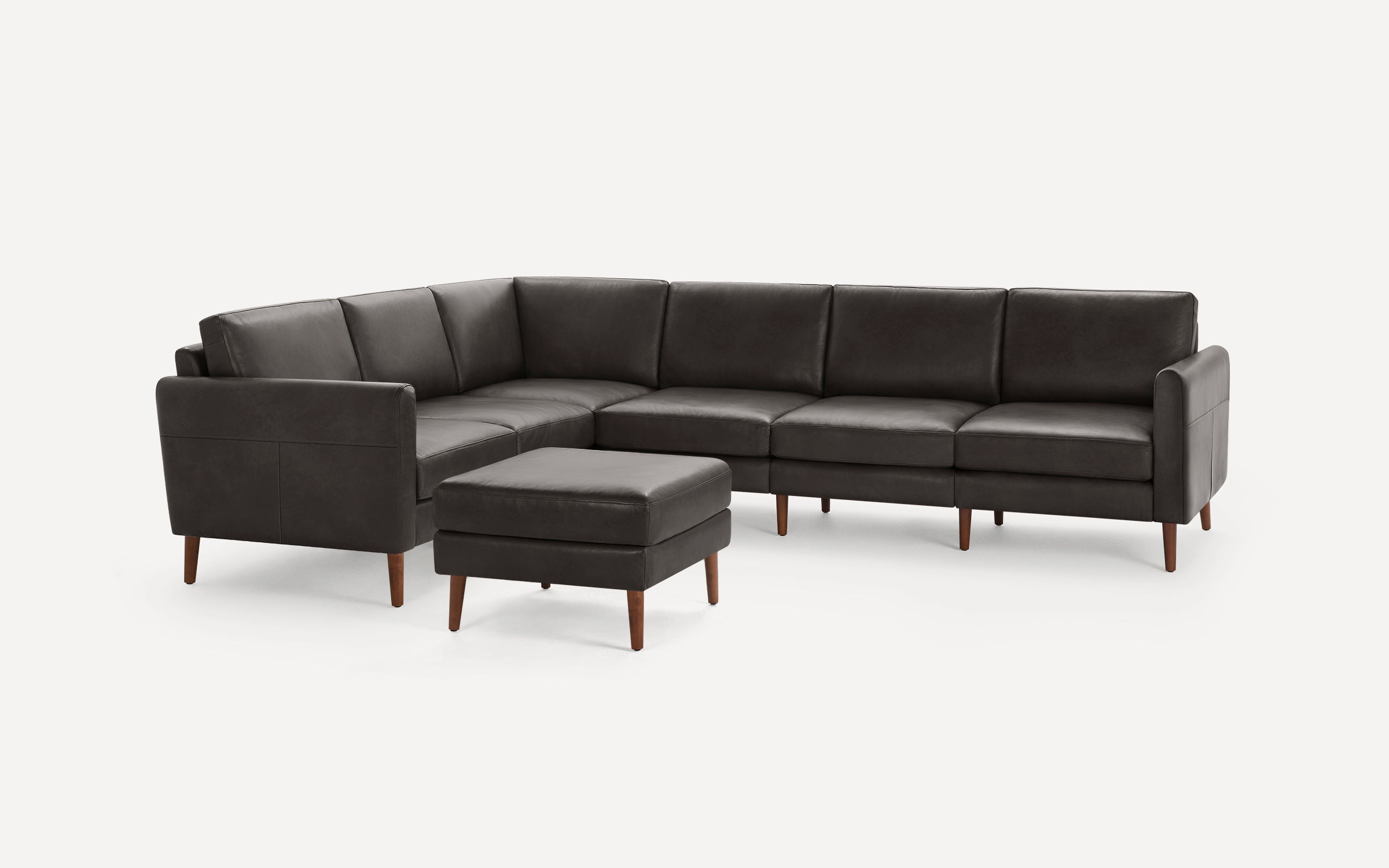 Dark gray leather L-shaped sectional sofa with separate matching ottoman, supported by tapered wooden legs.