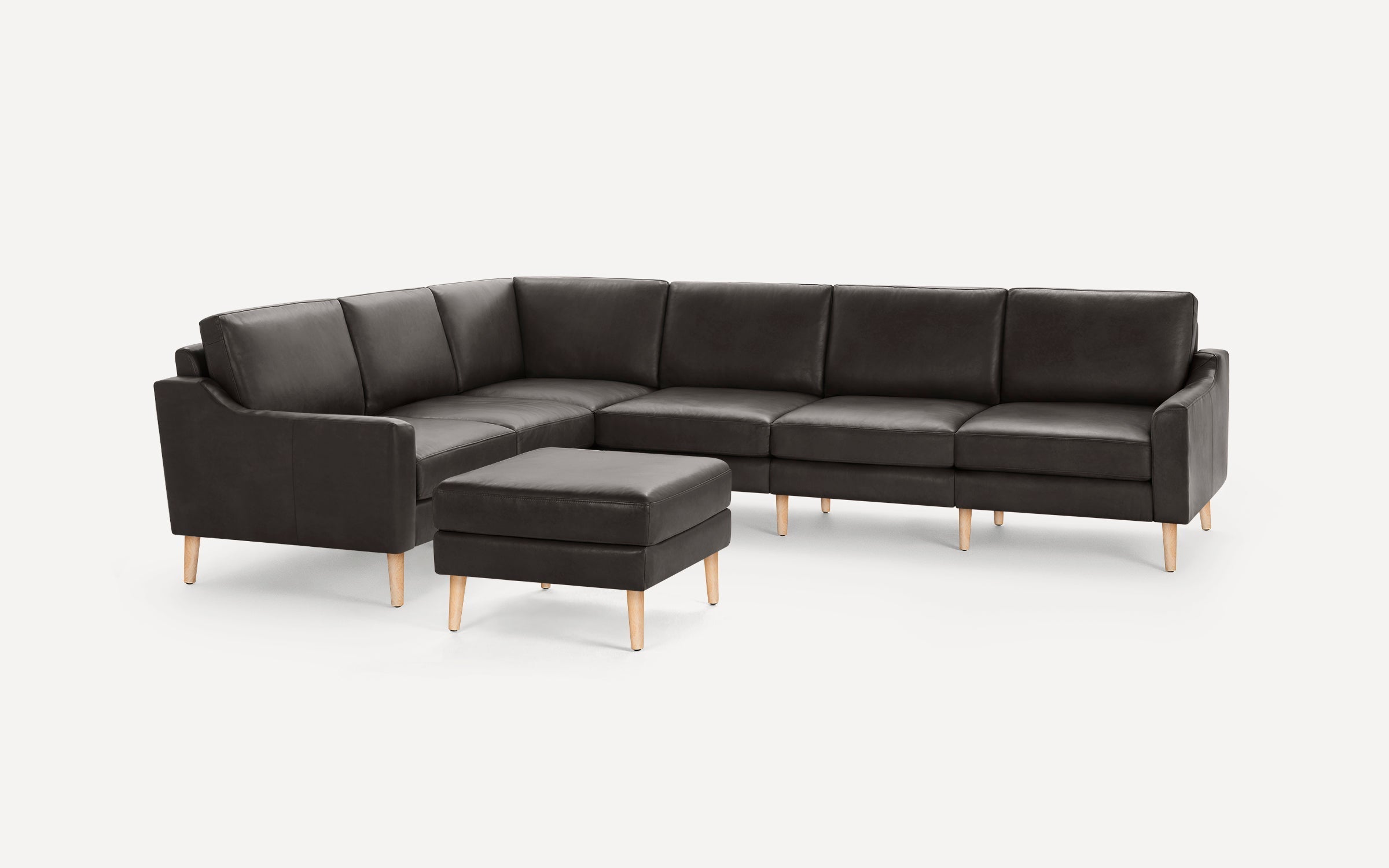 Dark gray L-shaped sectional sofa with wooden legs and matching square ottoman on white background.