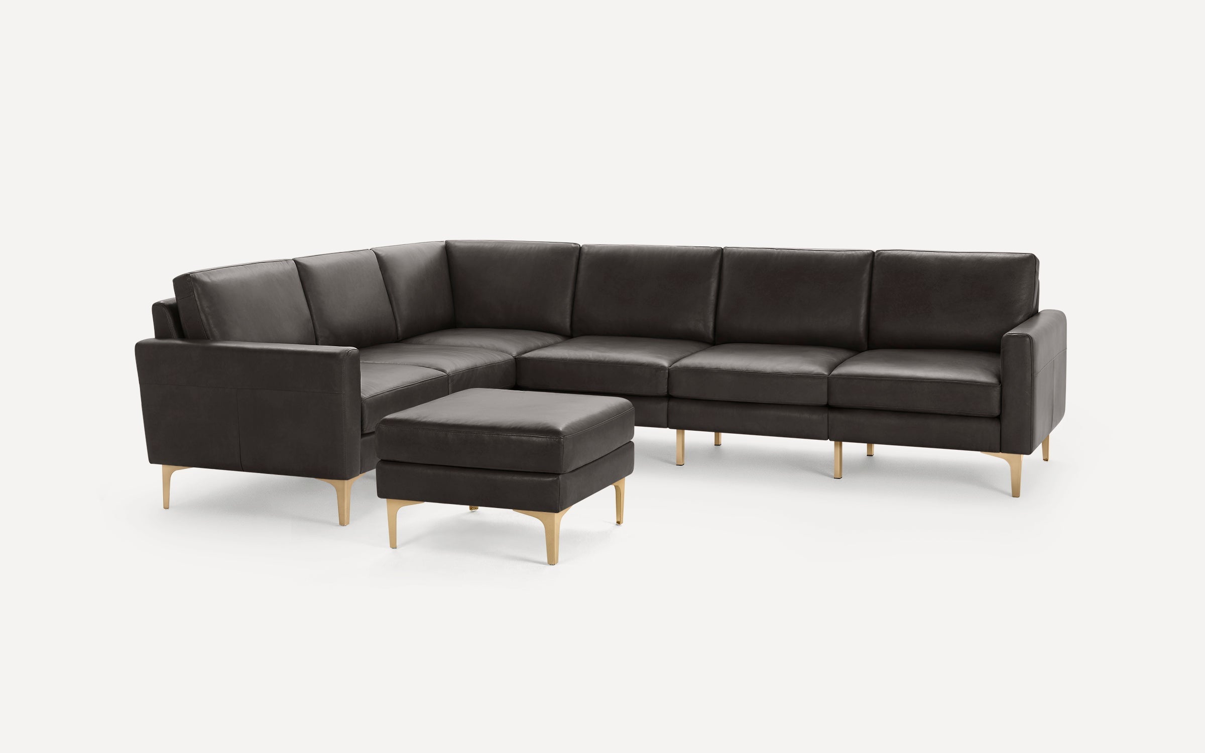 Dark gray leather L-shaped sectional sofa with matching ottoman and gold-toned metal legs, set against a plain white background.