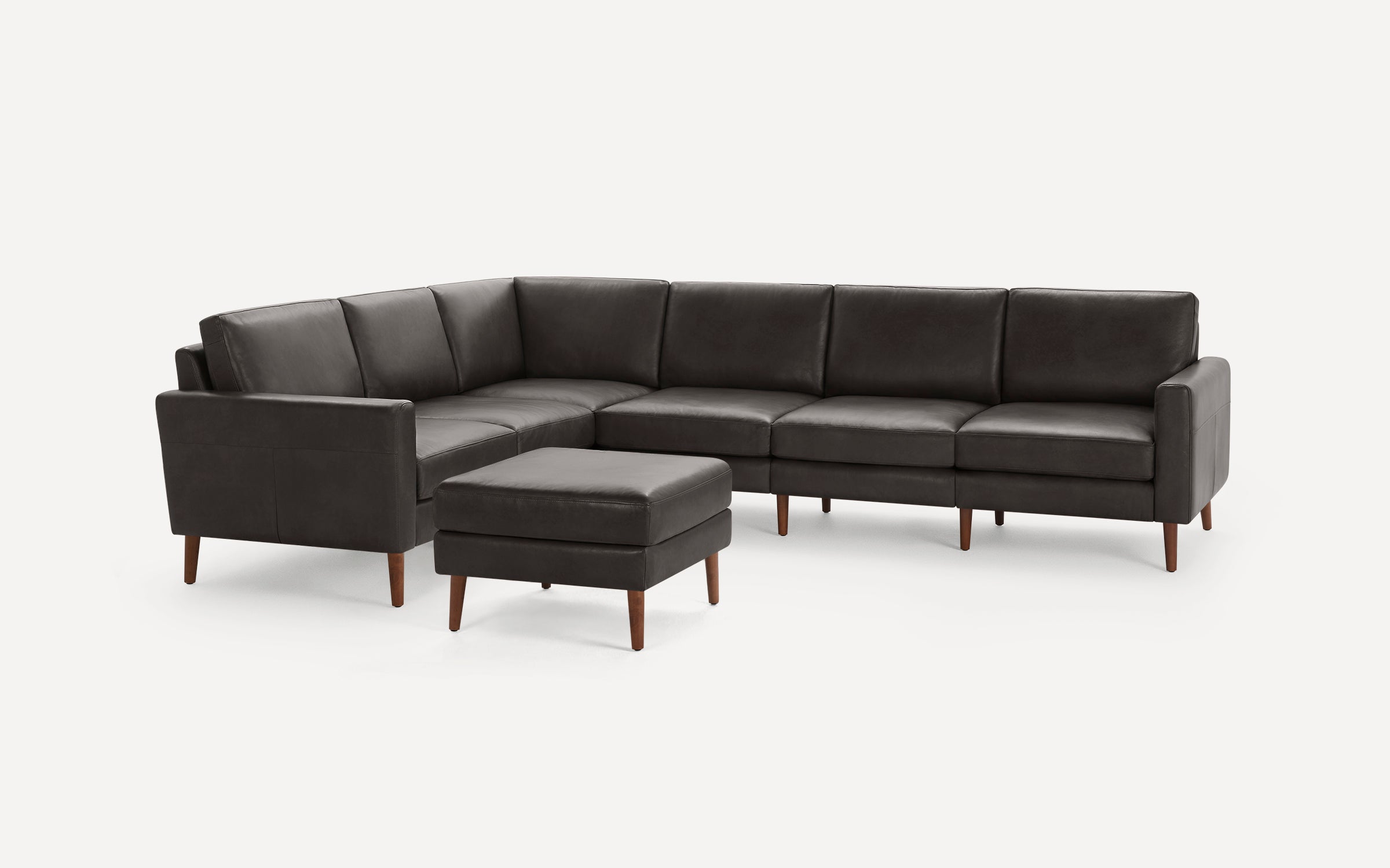 Dark gray leather sectional sofa with matching ottoman, featuring wooden legs and clean, modern design against a white background.