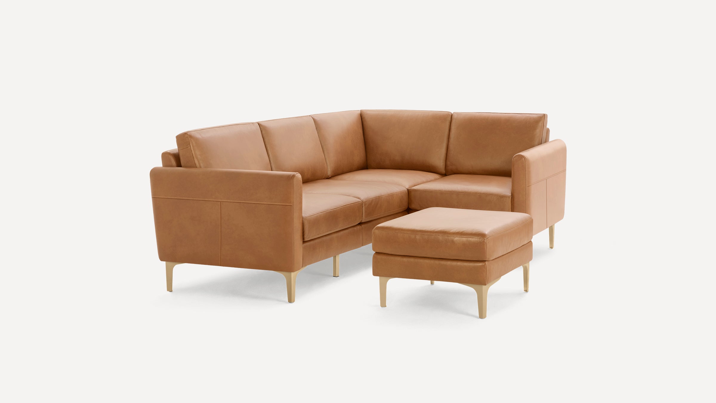 Modern tan leather sectional sofa with gold metal legs and matching ottoman on white background.