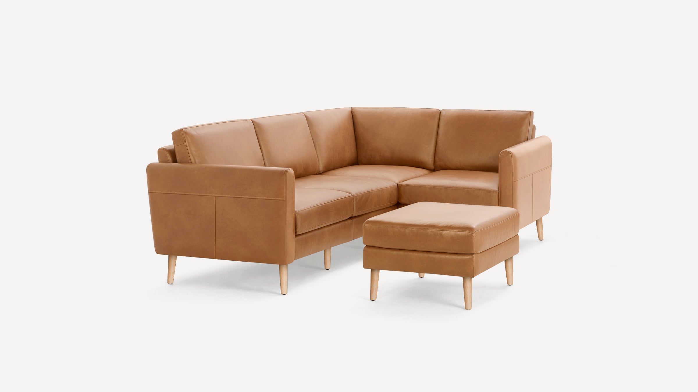 Tan leather sectional sofa with matching ottoman, featuring clean lines and wooden legs on a white background.